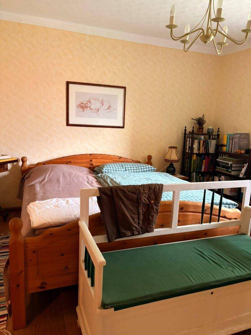 Helles Schlafzimmer mit Holzbett, gemusterter Tapete und traditionellen Möbeln.