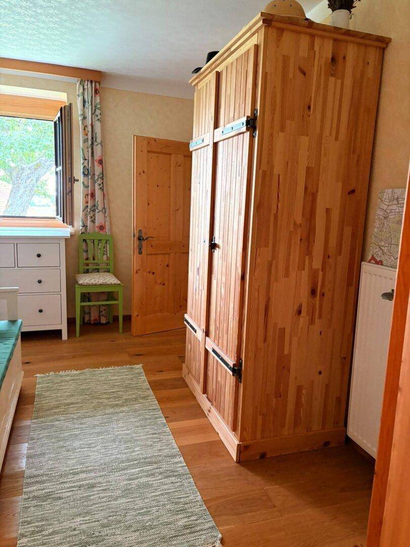 Schlafzimmer mit großem Holzschrank, Holzboden und Fenster mit Blick ins Grüne.