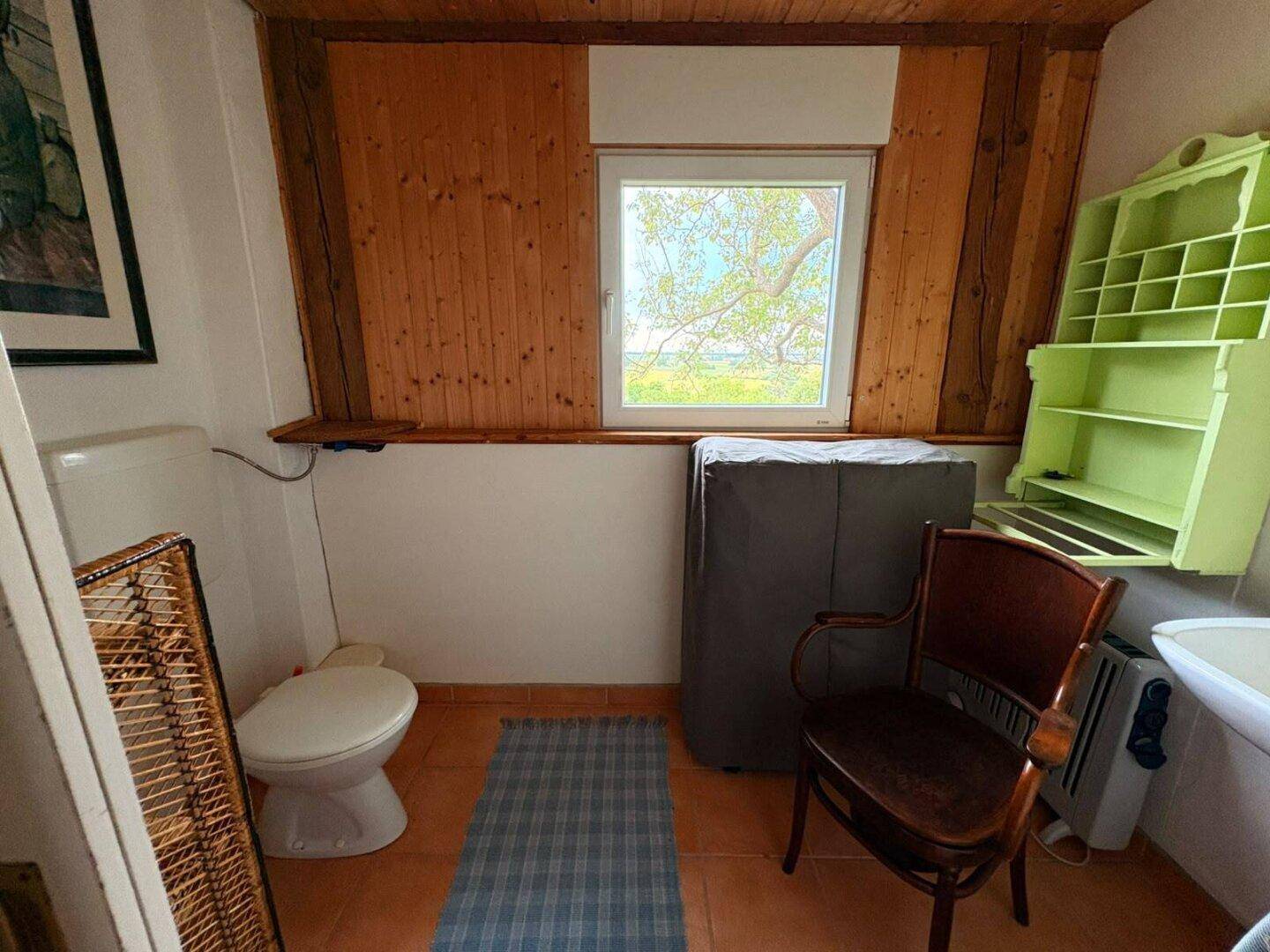 Kleines WC mit Fenster, Toilette und Holzvertäfelung unter der Dachschräge.