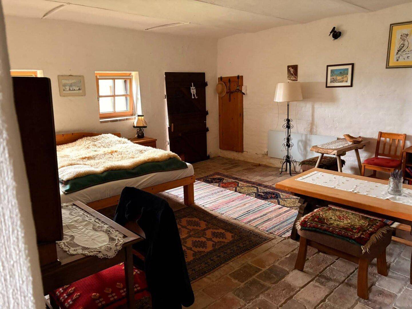 Schlafzimmer mit Bett, Tisch und traditionellen Teppichen auf Fliesenboden, rustikal eingerichtet.