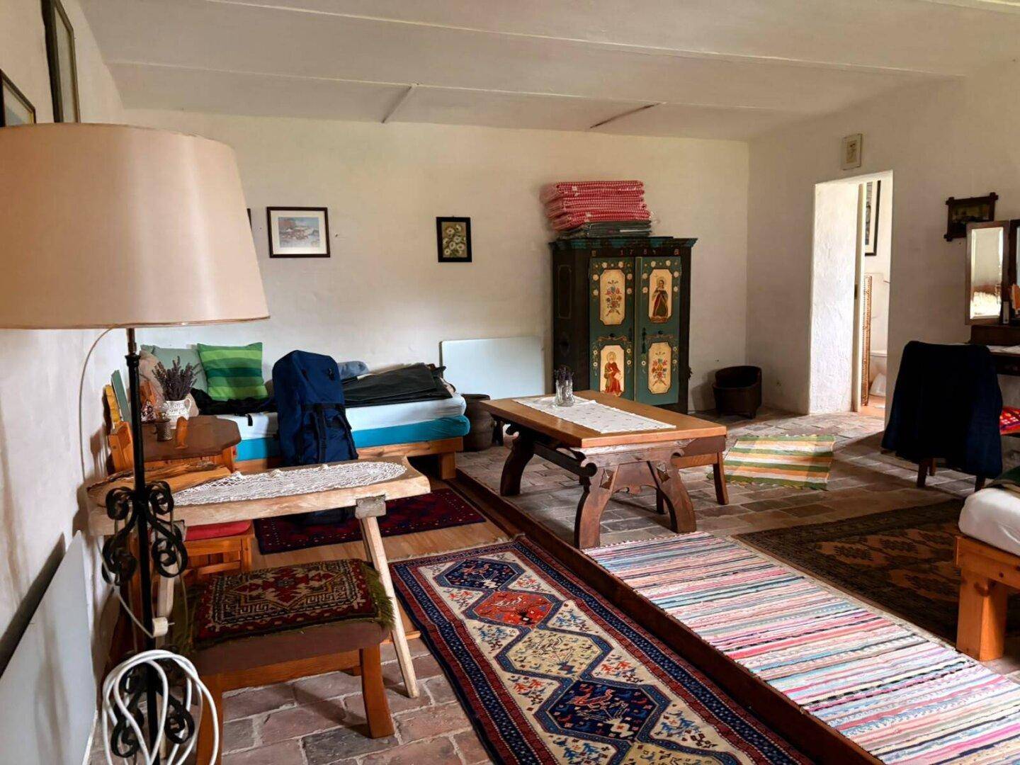Wohnzimmer mit Sofa, Tisch und traditionellen Teppichen auf Fliesenboden, rustikal eingerichtet.