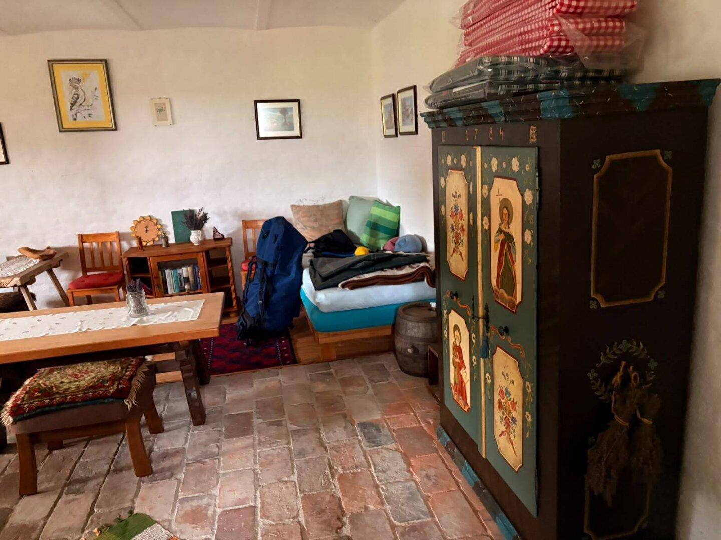 Rustikaler Wohnbereich mit Ziegelboden, Holztisch und einem traditionellen bemalten Schrank.