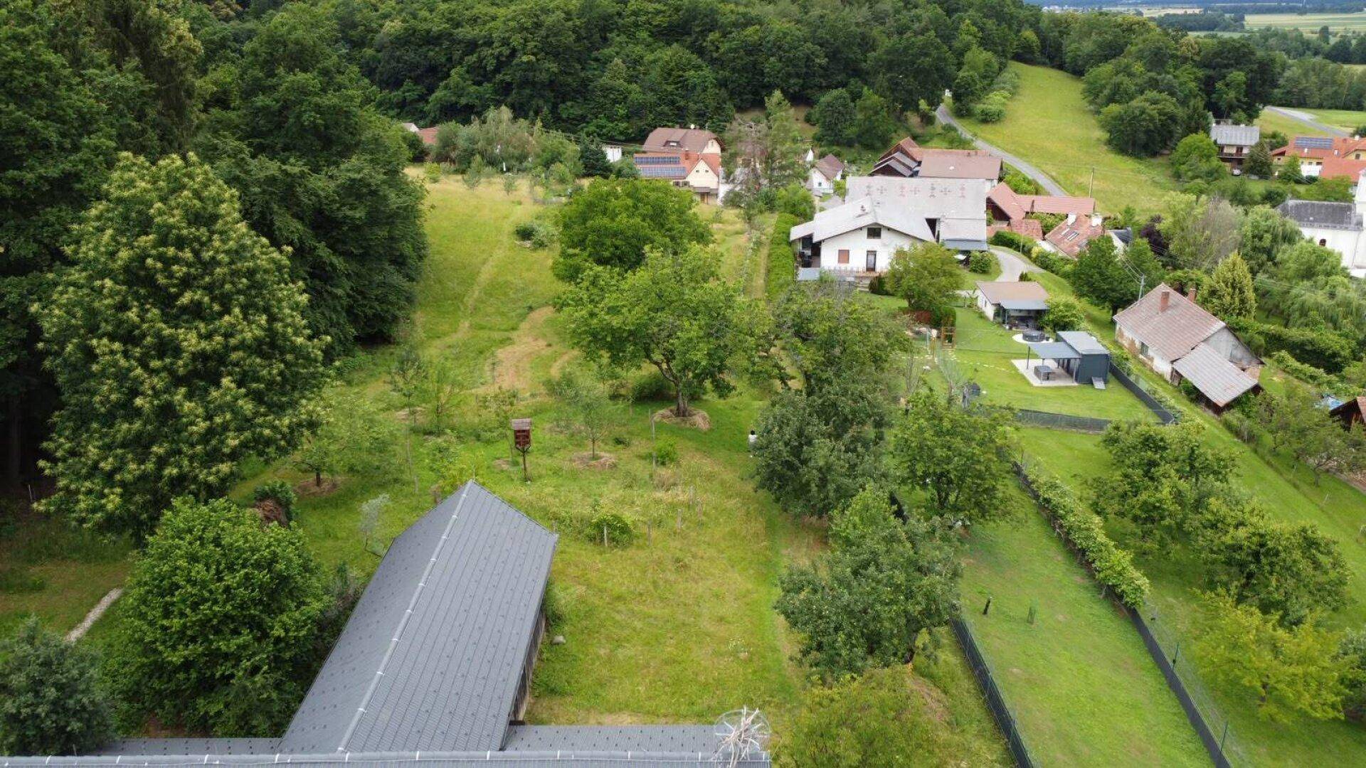 Weitläufige Luftaufnahme des Anwesens eingebettet in eine hügelige, grüne Landschaft mit weiteren Häusern.