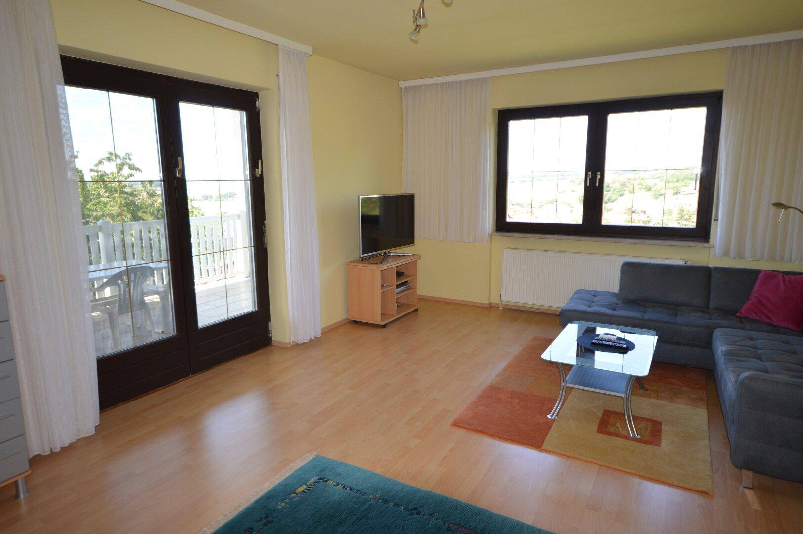 Helles Wohnzimmer mit Laminatboden, Sofa und Zugang zu einem sonnigen Balkon.