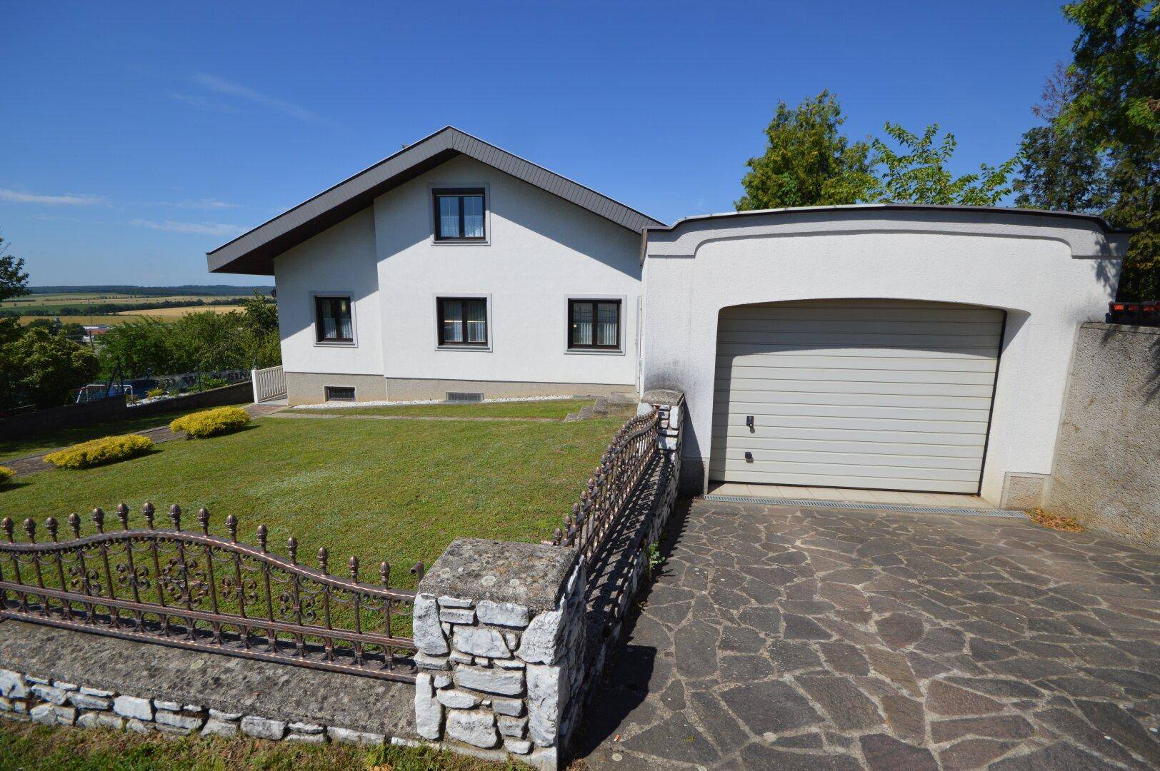 Einfamilienhaus mit integrierter Garage und gepflasterter Auffahrt unter blauem Himmel.