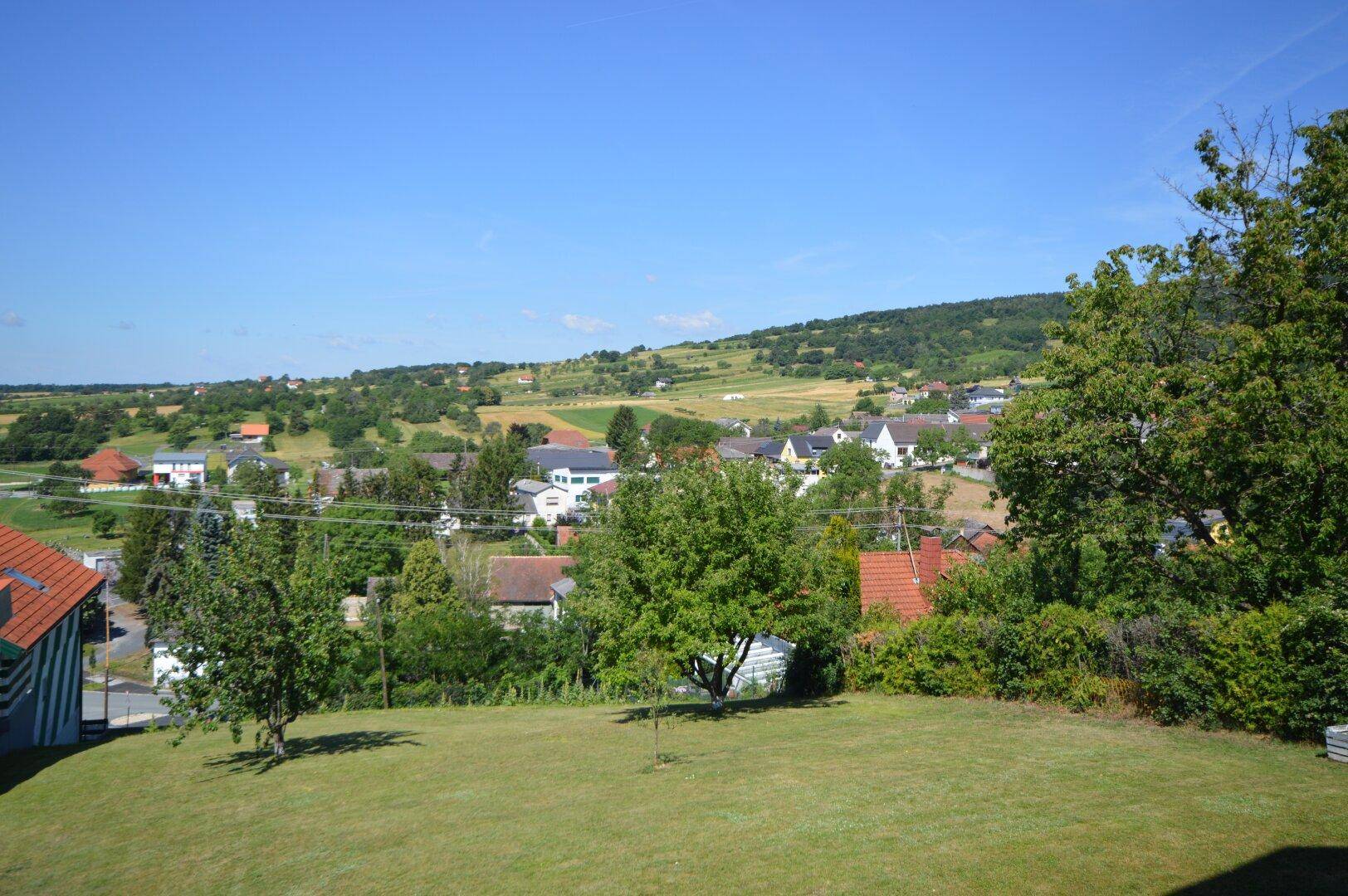 Weitläufiger Blick über die grüne Landschaft mit verstreuten Häusern und Hügeln.
