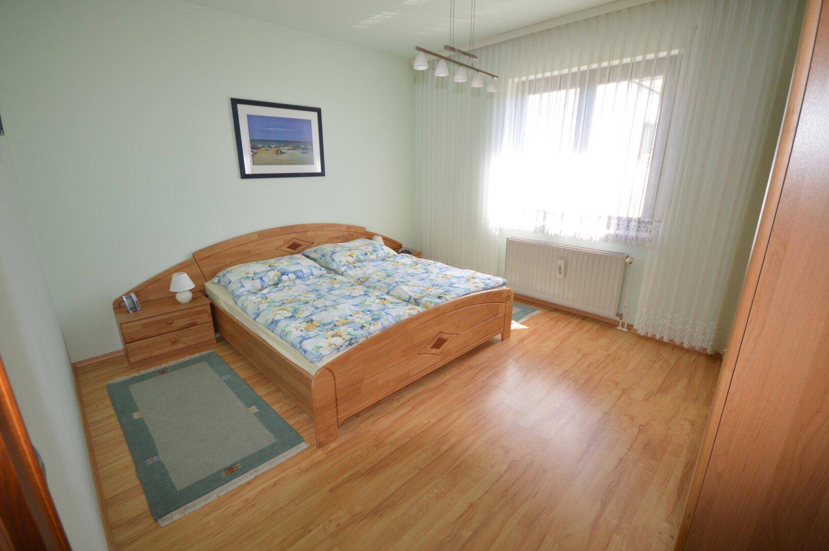 Schlafzimmer mit hellem Laminatboden, Doppelbett und großem Fenster für viel Licht.