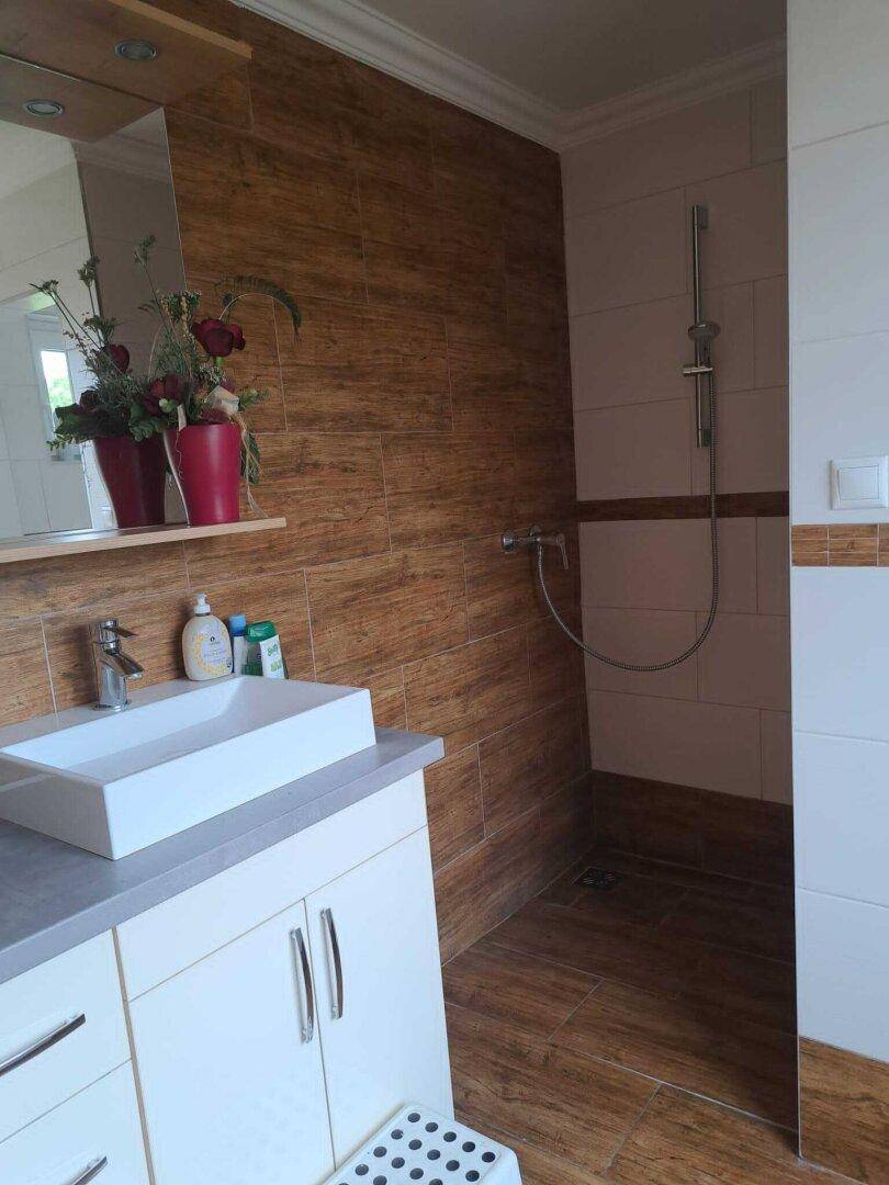 Modernes Badezimmer mit Aufsatzwaschbecken, Spiegel und Duschbereich mit Holzoptikfliesen.