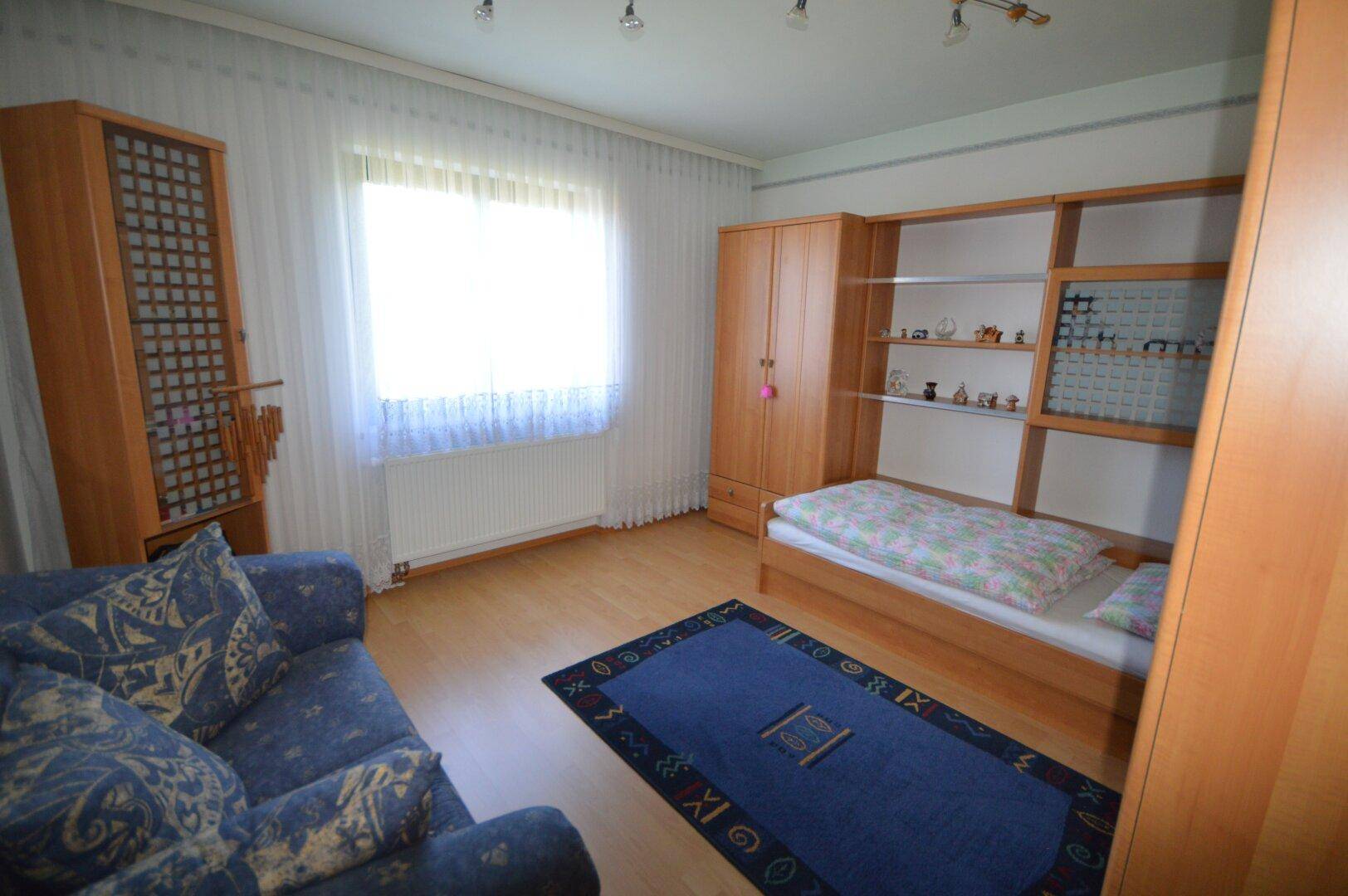 Freundliches Schlafzimmer mit Einzelbett, Schrank und einem blauen Teppich.