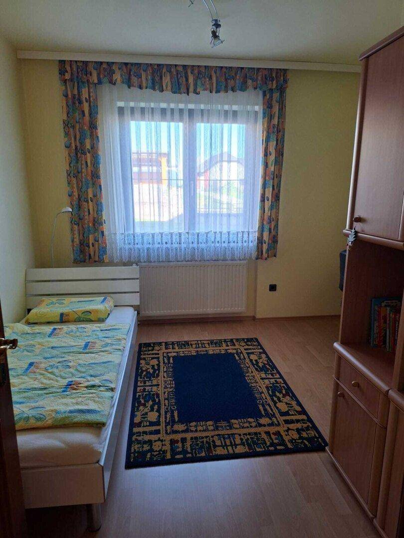 Helles Schlafzimmer mit Einzelbett, Holzmöbeln und farbenfrohen Vorhängen.