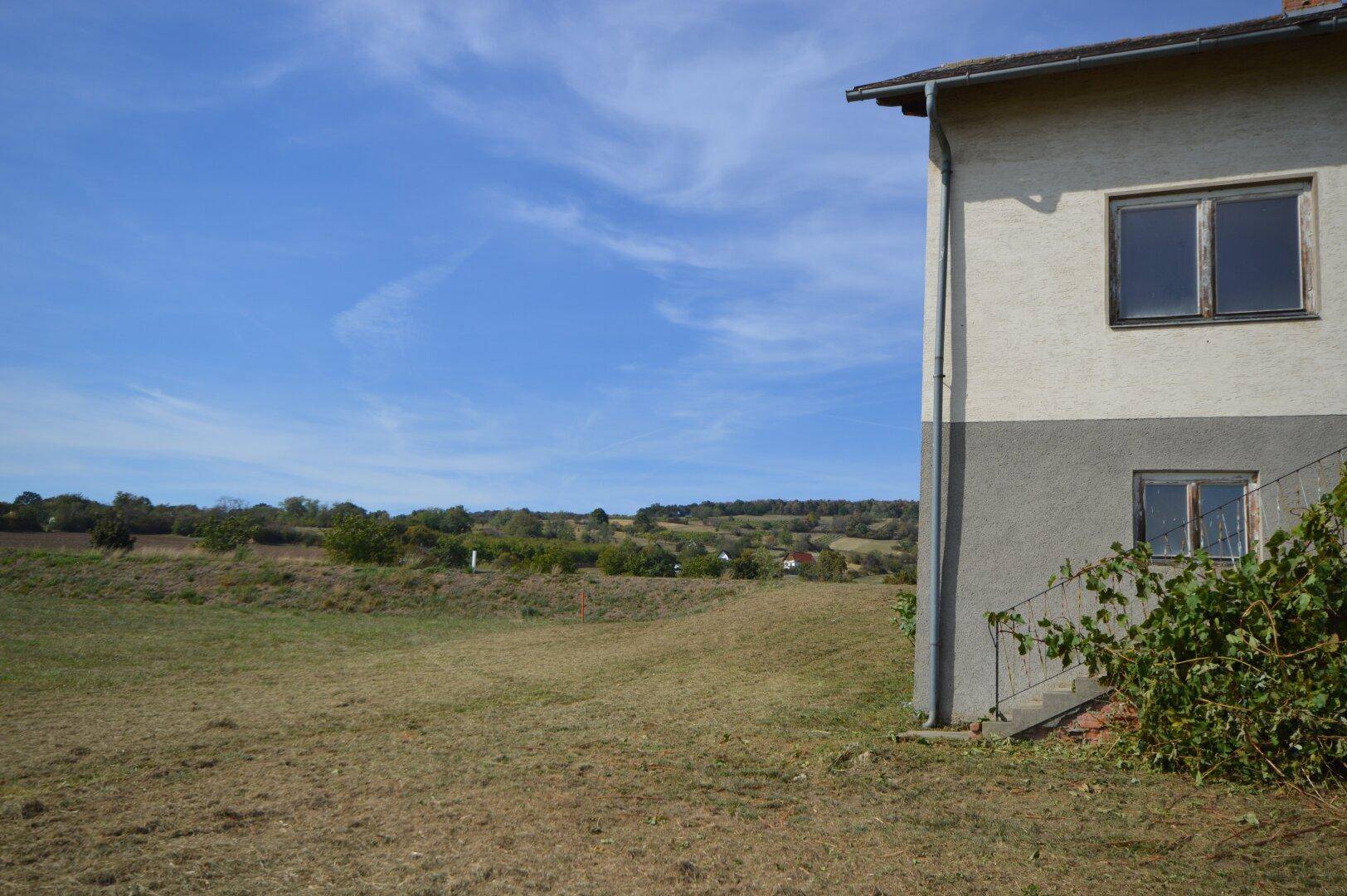 Blick auf die hügelige Landschaft und die Seite des Hauses mit einfacher Fassade.