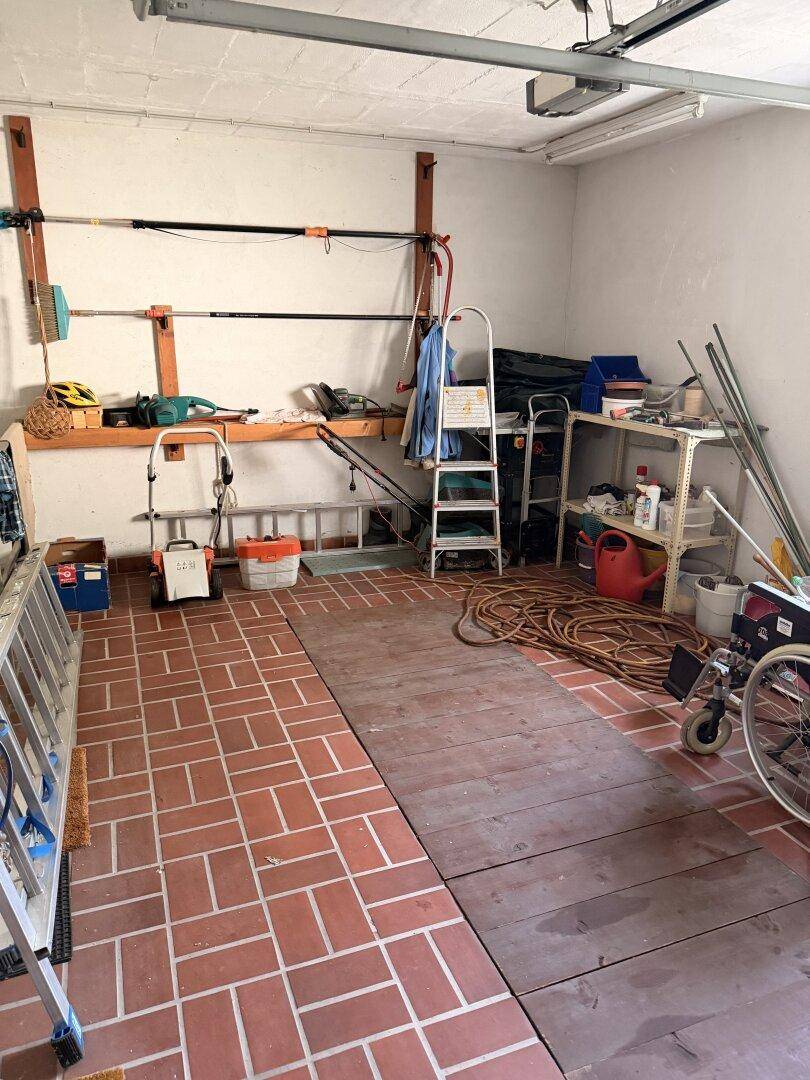 Garage mit Werkzeugen, Leitern und Lagerflächen, ausgestattet mit Fliesenboden und Holzplatten.