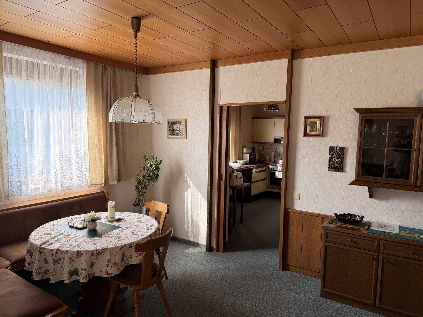 Essbereich mit Holztisch, Eckbank und Blick in die Küche, geprägt von Holzvertäfelung und Teppichboden.