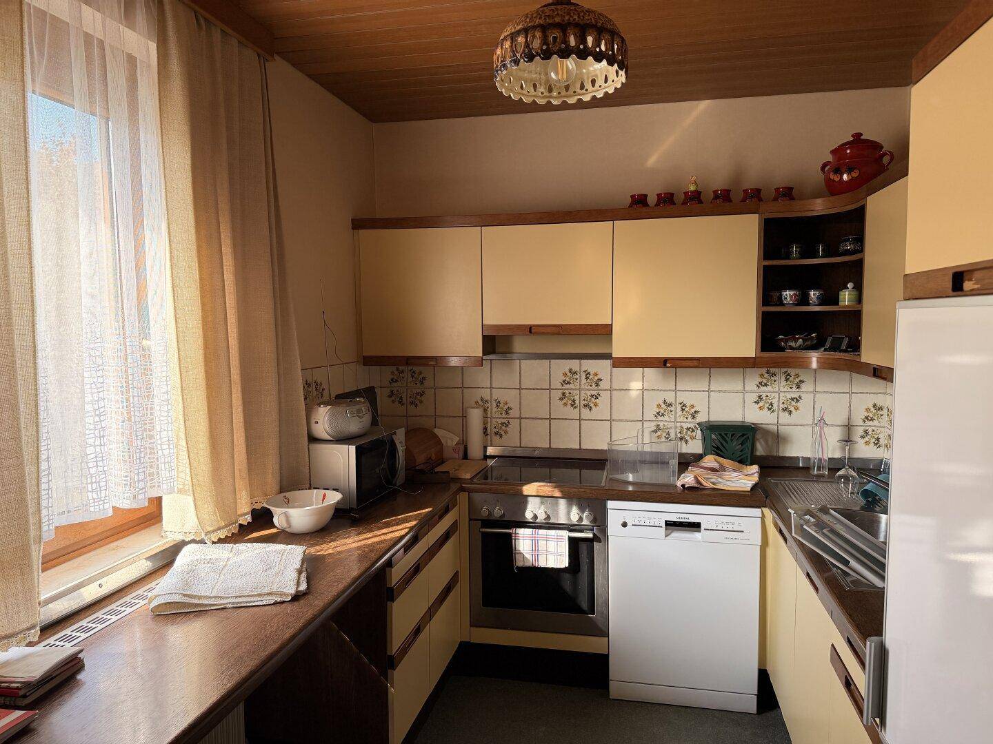 Helle Küche im Landhausstil mit gelben Schränken, Fliesenrückwand und Fenster mit viel Tageslicht.