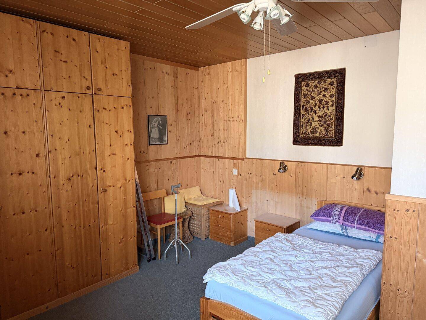 Schlafzimmer mit Holzvertäfelung, Einbauschränken und einem Deckenventilator, ausgestattet mit Teppichboden.