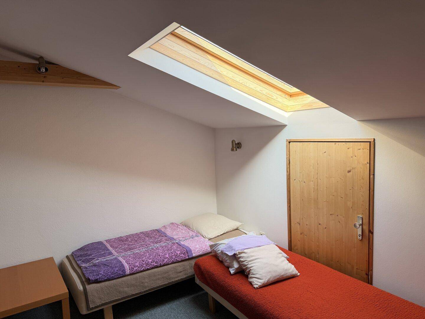 Dachgeschoss-Schlafzimmer mit zwei Einzelbetten, Dachfenster und schrägen Wänden für natürliches Licht.
