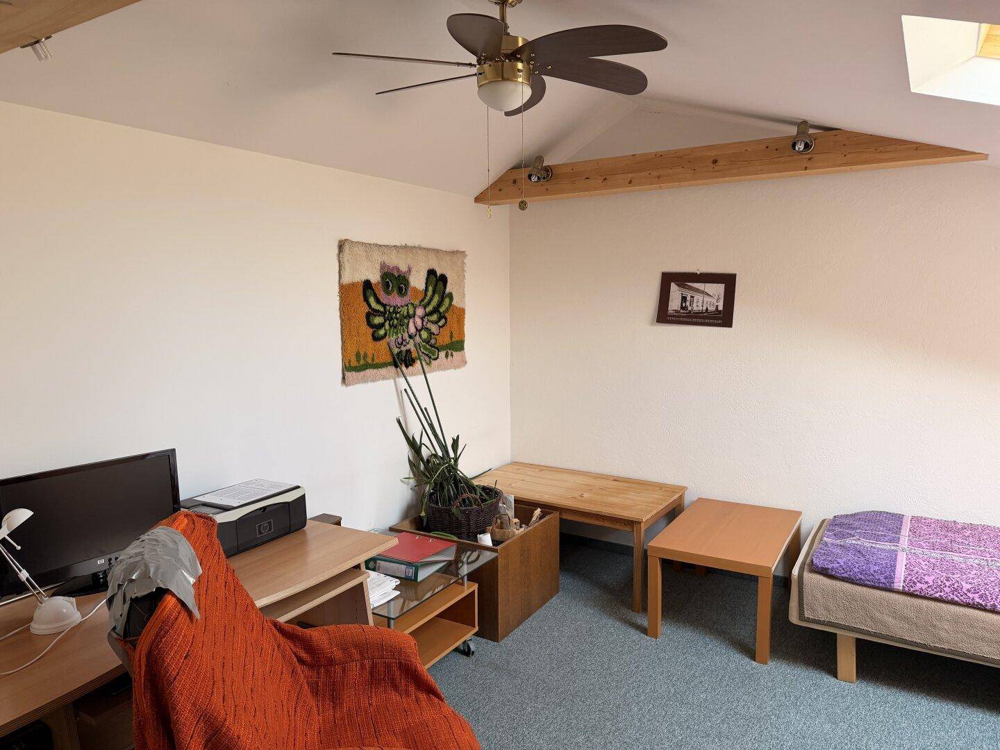 Dachgeschosszimmer mit Deckenventilator, Schreibtisch und Einzelbett, unter einer schrägen Decke.