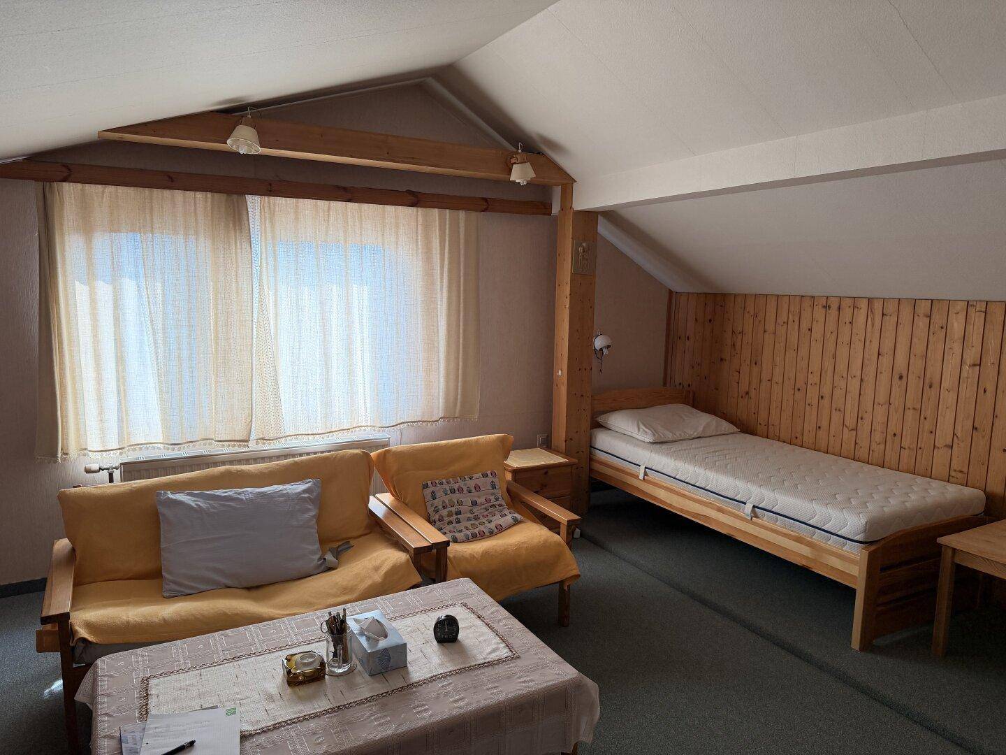 Gemütliches Dachgeschosszimmer mit Holzvertäfelung, Einzelbett und Sofa, unter einer schrägen Decke.