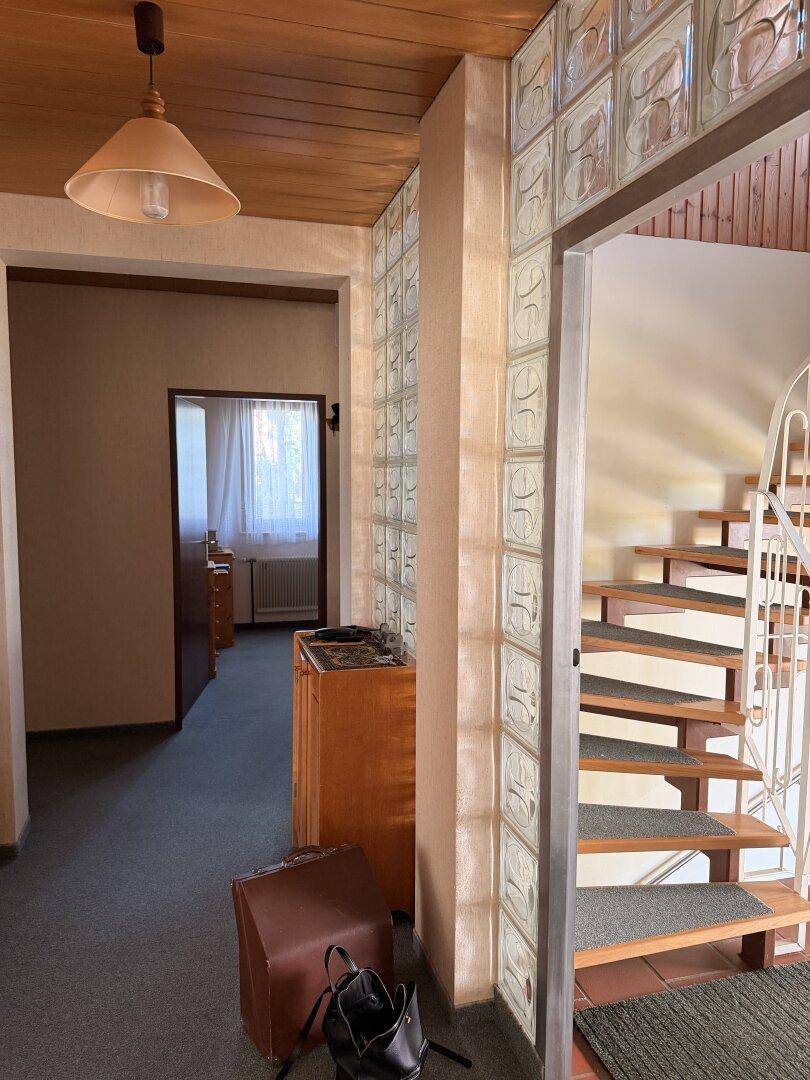 Flur mit Glasbausteinwand, Holzdecke und Treppe zum Obergeschoss, ausgestattet mit Teppichboden.