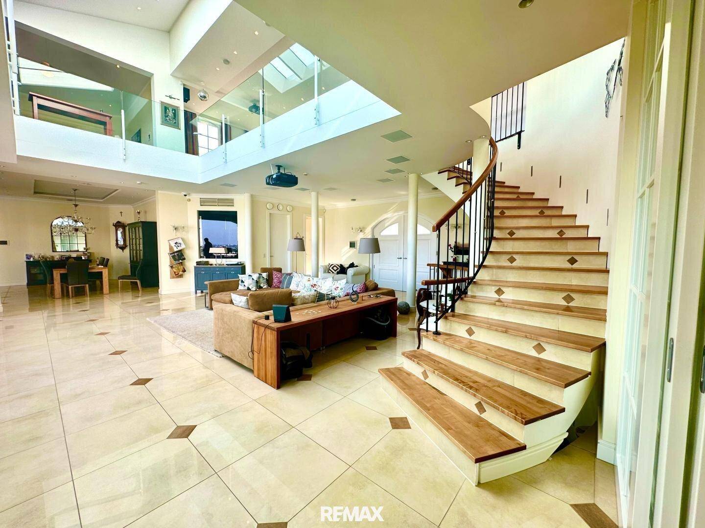 Geräumiger Wohnbereich mit eleganter Holztreppe, Fliesenboden und Zugang zu weiteren Räumen.