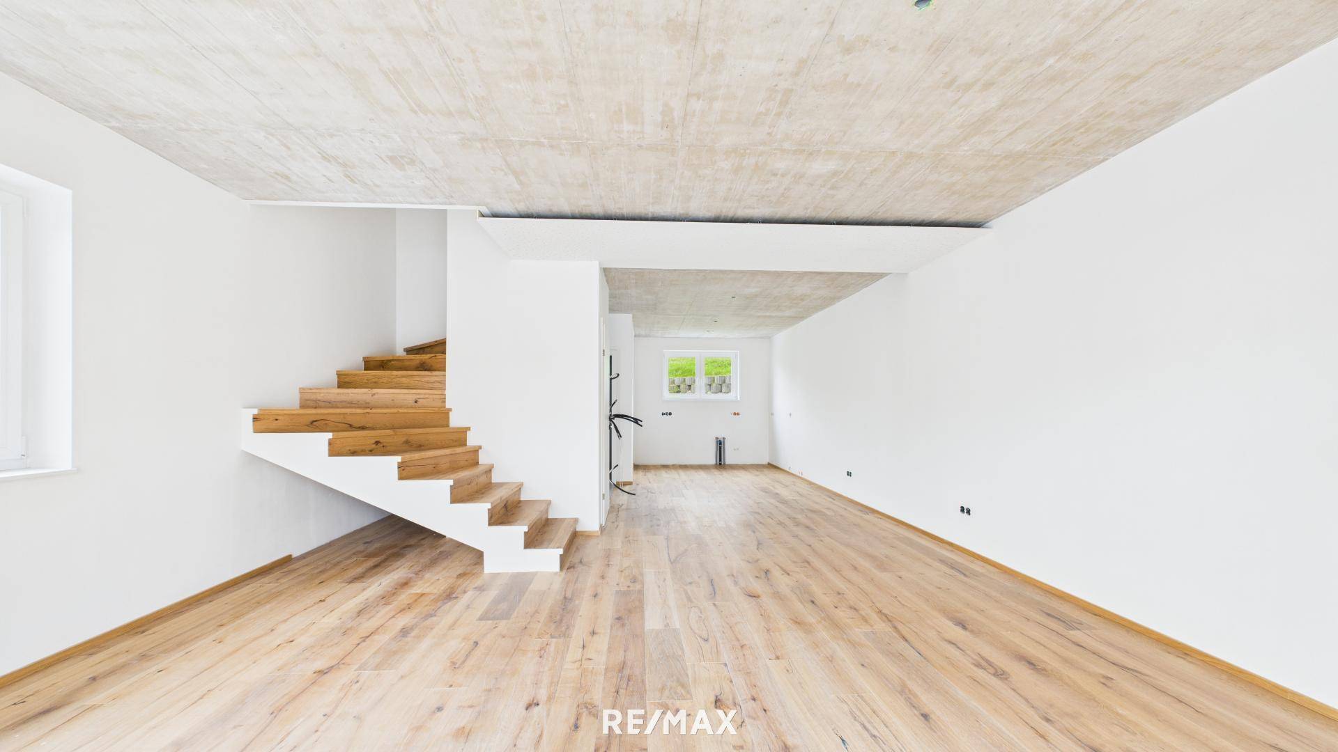 Heller Wohnbereich im Neubau mit Holzboden, weißen Wänden und einer modernen Holztreppe.