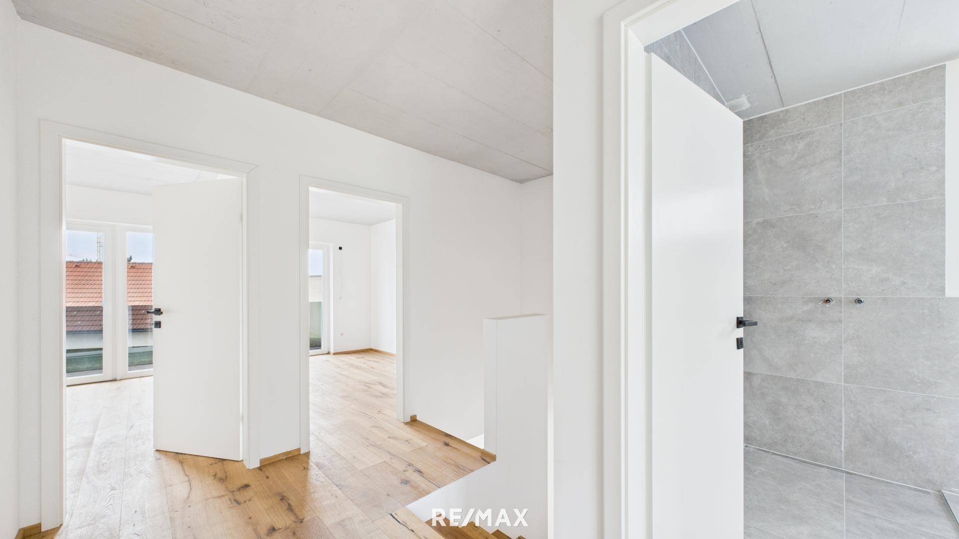 Heller Flur mit Holzboden, der zu weiteren Zimmern und einem modern gefliesten Badezimmer führt.