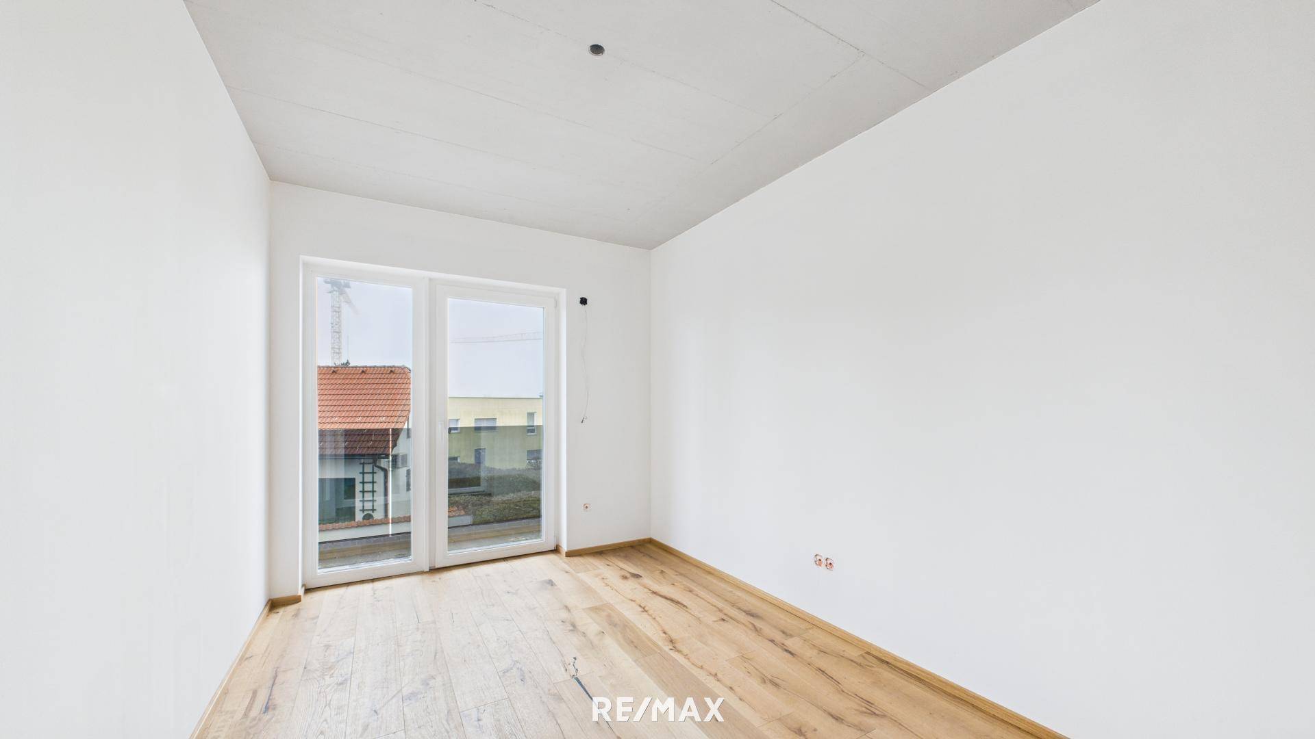 Leeres Schlafzimmer mit Holzboden und Zugang zu einem Balkon oder einer Terrasse durch große Fenstertüren.