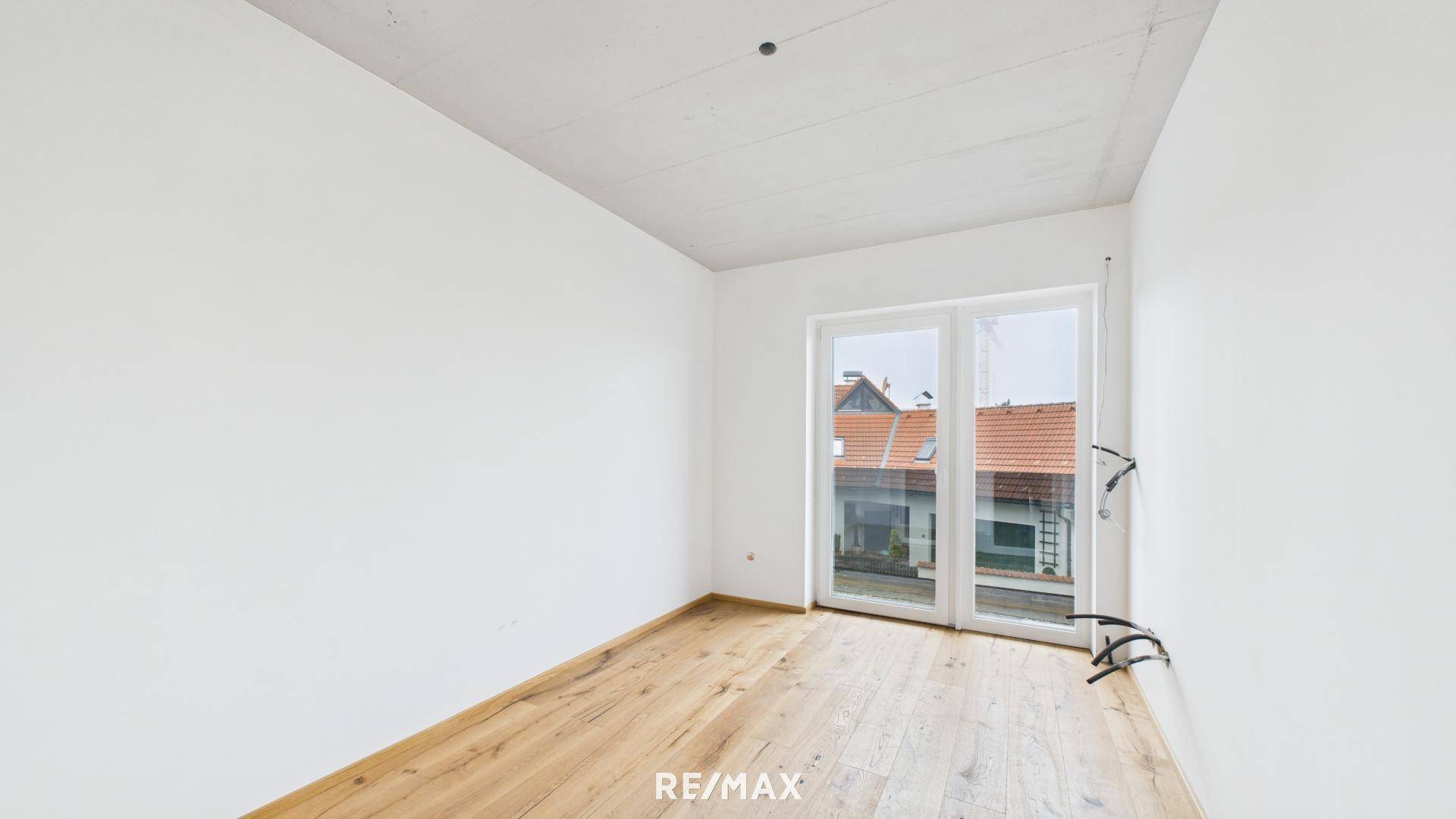 Unmöbliertes Schlafzimmer mit Holzboden und großer Fenstertür für viel Tageslicht und Ausblick.