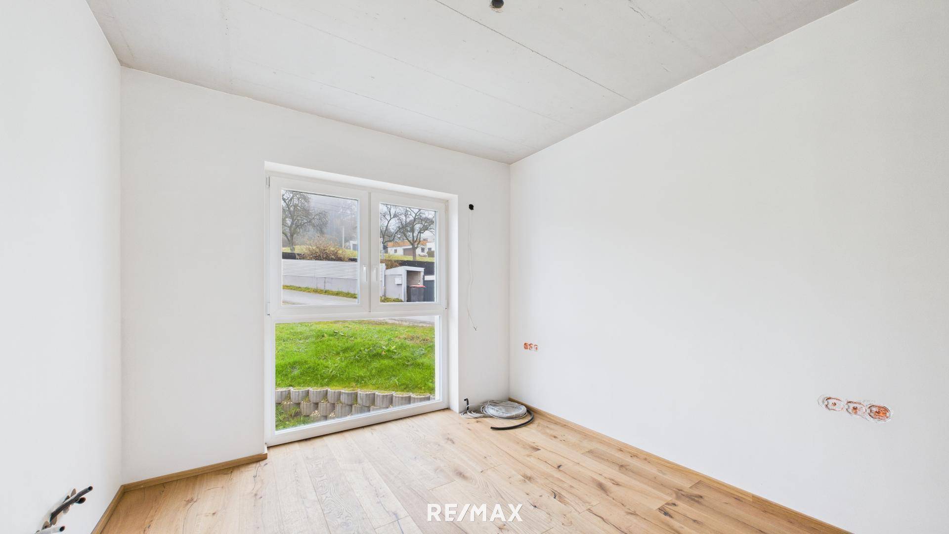 Helles Zimmer im Erdgeschoss mit Holzboden und direktem Zugang zum grünen Gartenbereich.