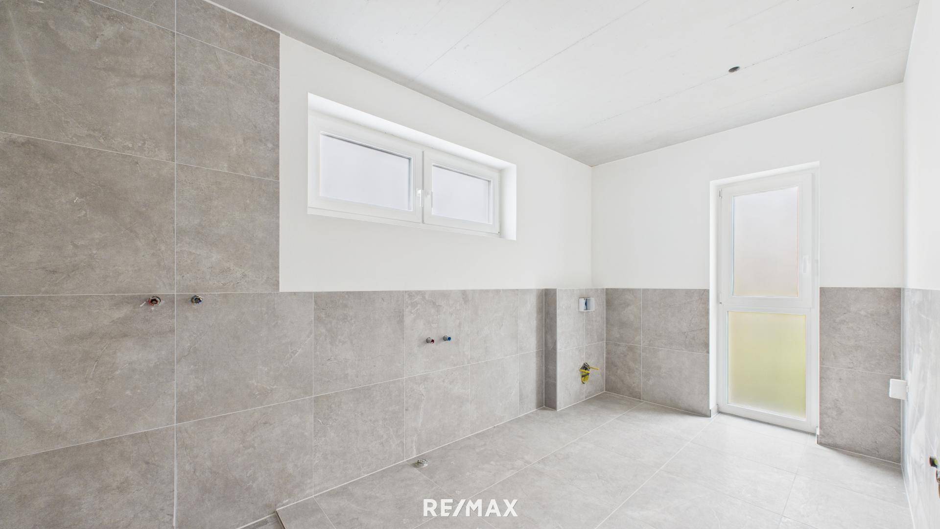 Unfertiges Badezimmer mit modernen grauen Fliesen an Wänden und Boden, bereit für Installationen.