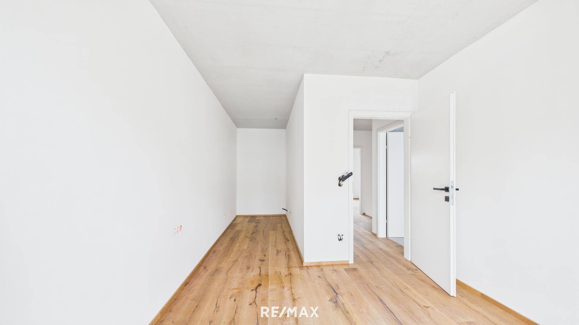 Langer, heller Flur mit Holzboden und weißen Wänden, der zu verschiedenen Räumen führt.