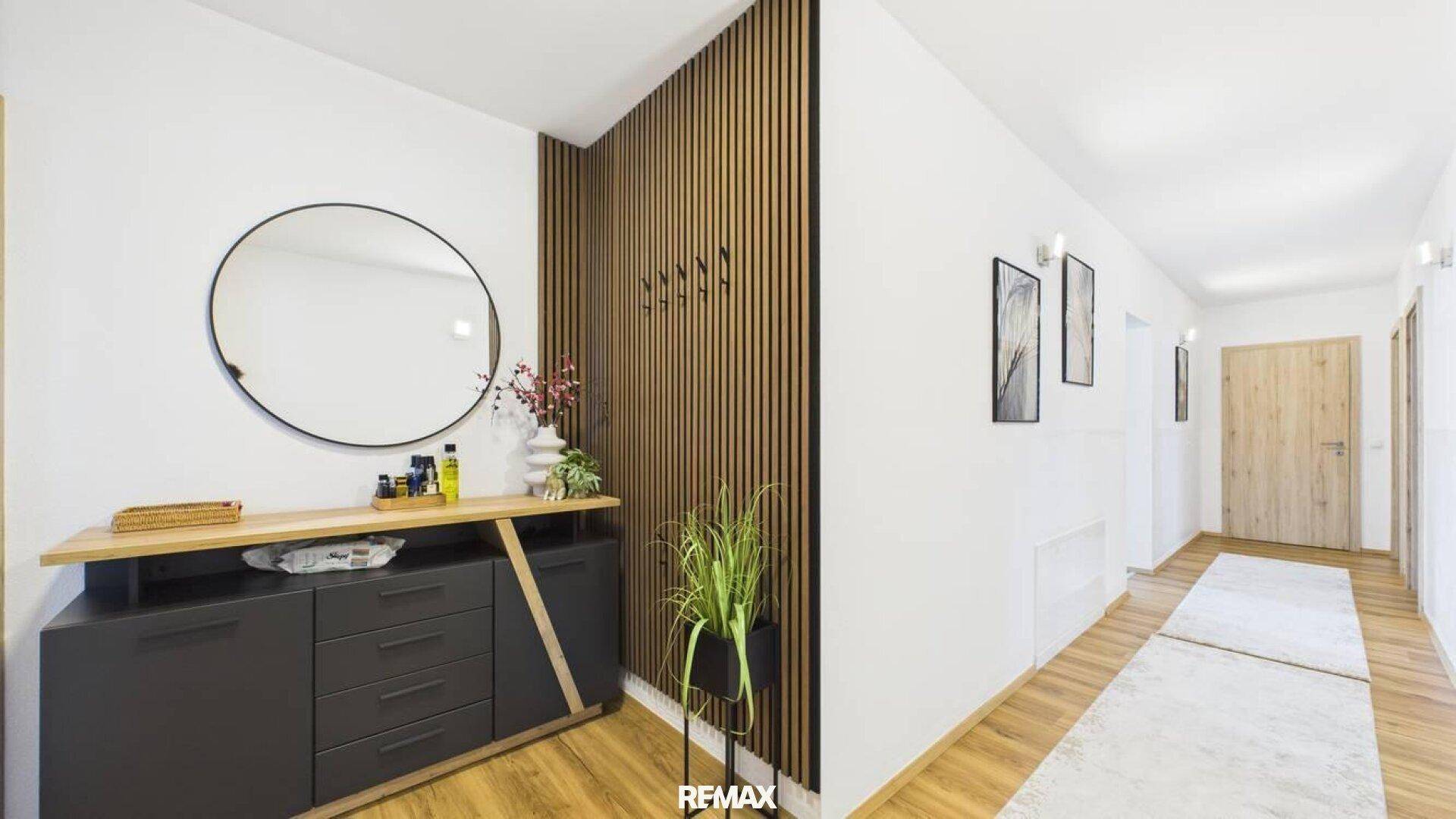 Eingangsbereich mit dekorativer Holzlamellenwand, rundem Spiegel und moderner Kommode.