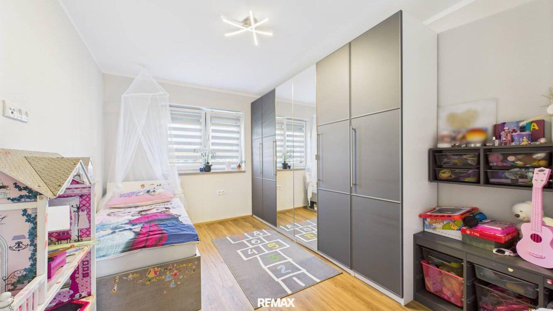 Kinderzimmer mit Einzelbett, großem Spiegelschrank und Spielbereich am Fenster.