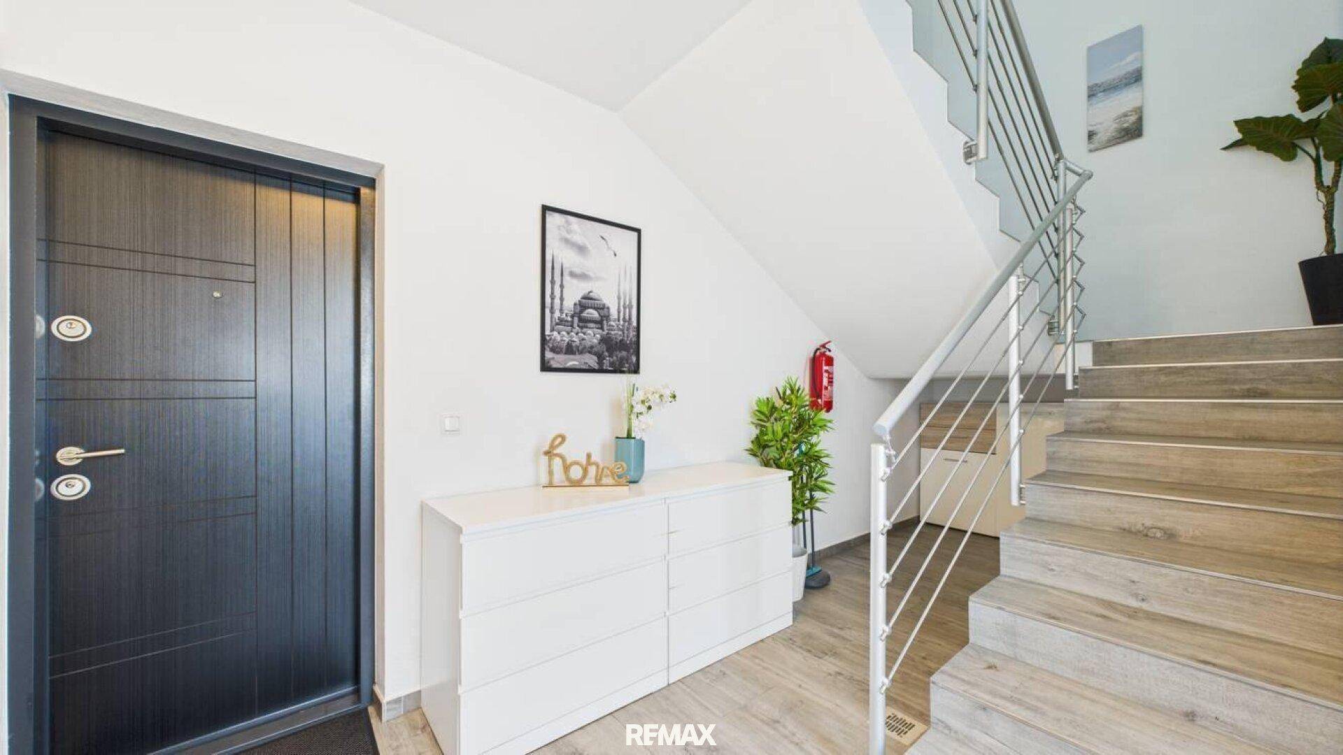 Heller Eingangsbereich mit Treppe, moderner Haustür und weißer Kommode.