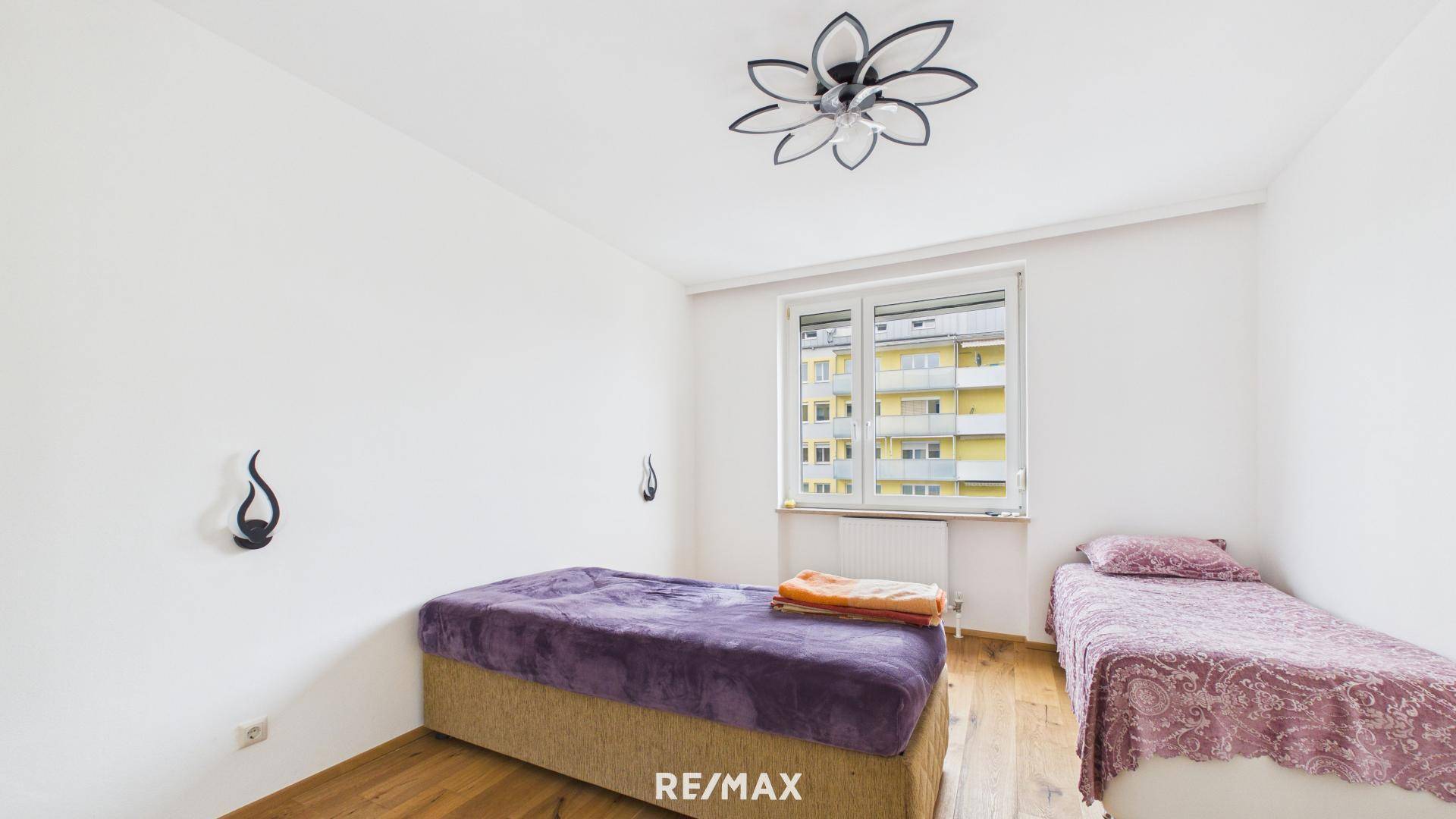 Schlafzimmer mit zwei Betten, Holzboden und Blick auf die umliegenden Gebäude.