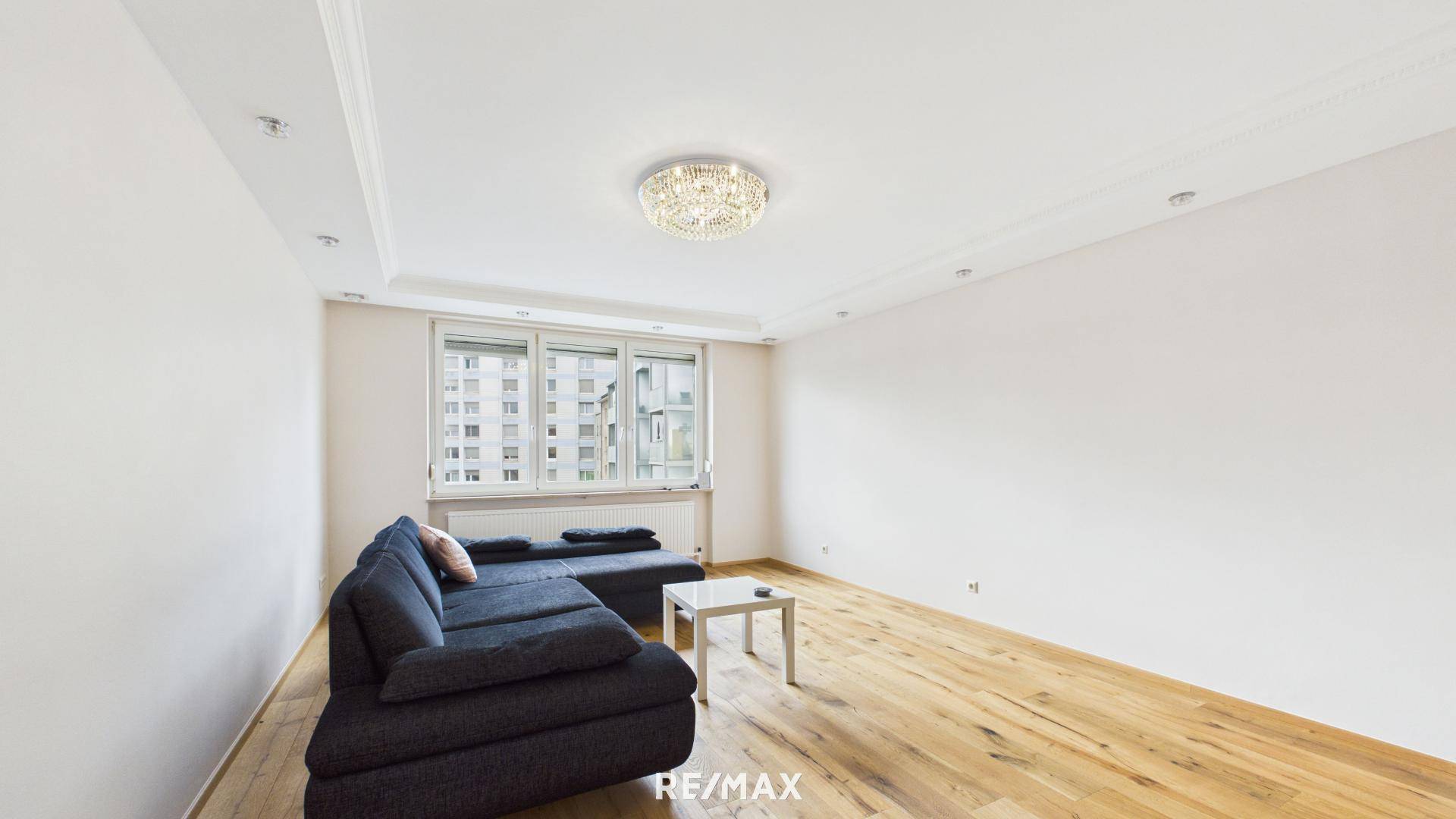 Helles Wohnzimmer mit Holzboden, großer Couch und Blick auf die umliegenden Gebäude.