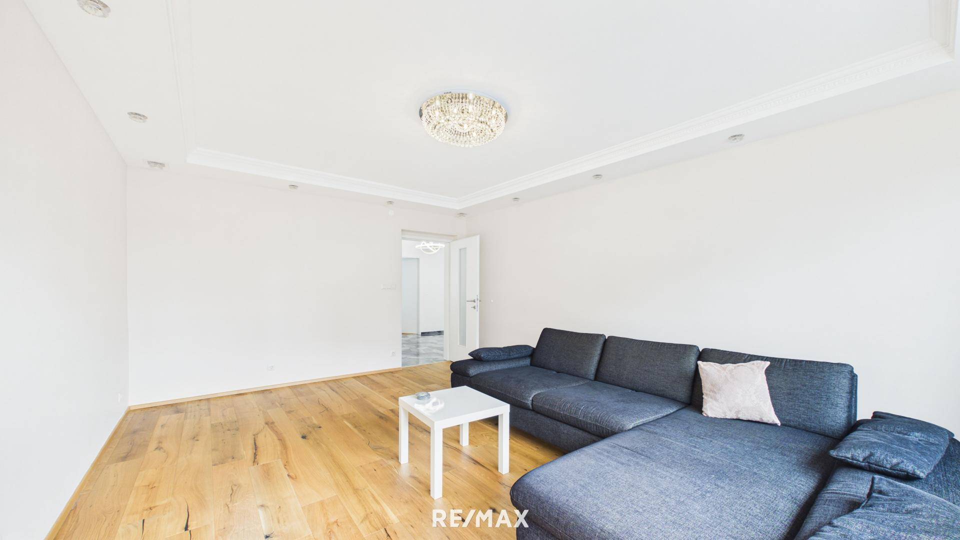 Geräumiges Wohnzimmer mit Holzboden, bequemer Couch und moderner Deckenbeleuchtung.