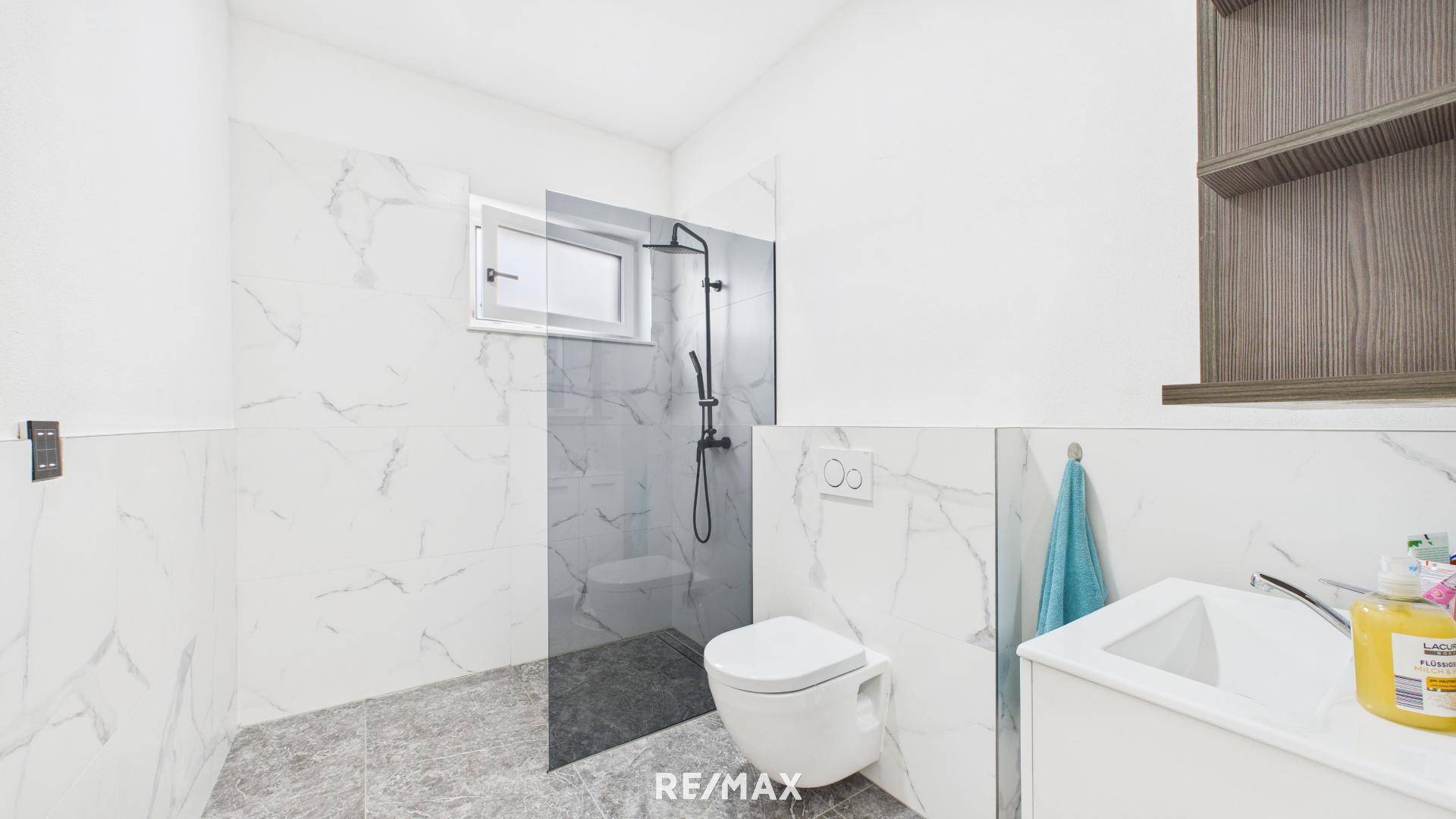 Modernes Badezimmer mit weißen Marmorfliesen, begehbarer Dusche und wandhängendem WC.