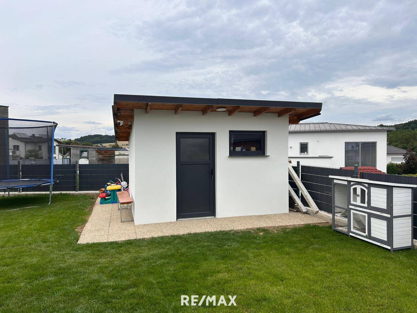 Kleiner Garten mit Geräteschuppen, Trampolin und Hühnerstall, umgeben von Rasenfläche.