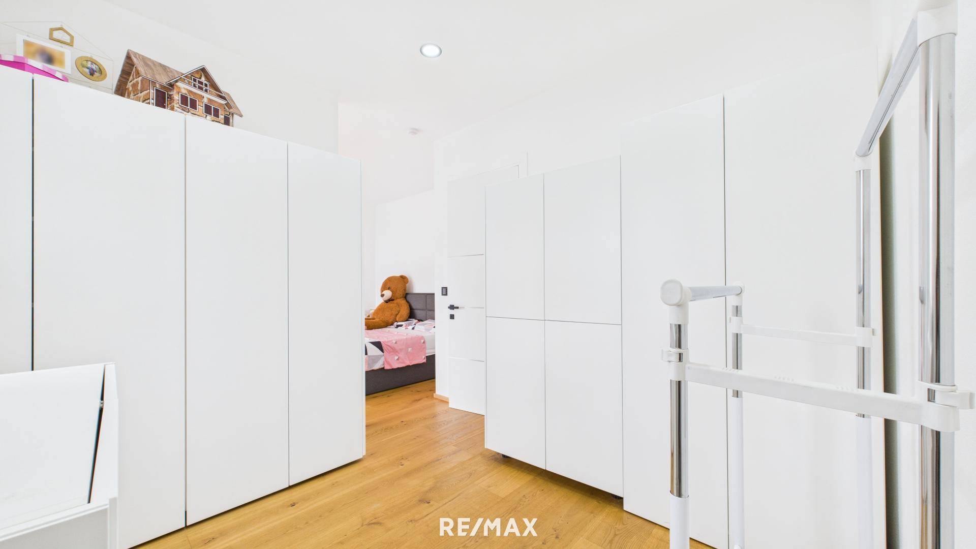 Ankleidebereich mit weißen Einbauschränken und Holzboden, der zu einem Schlafzimmer führt.