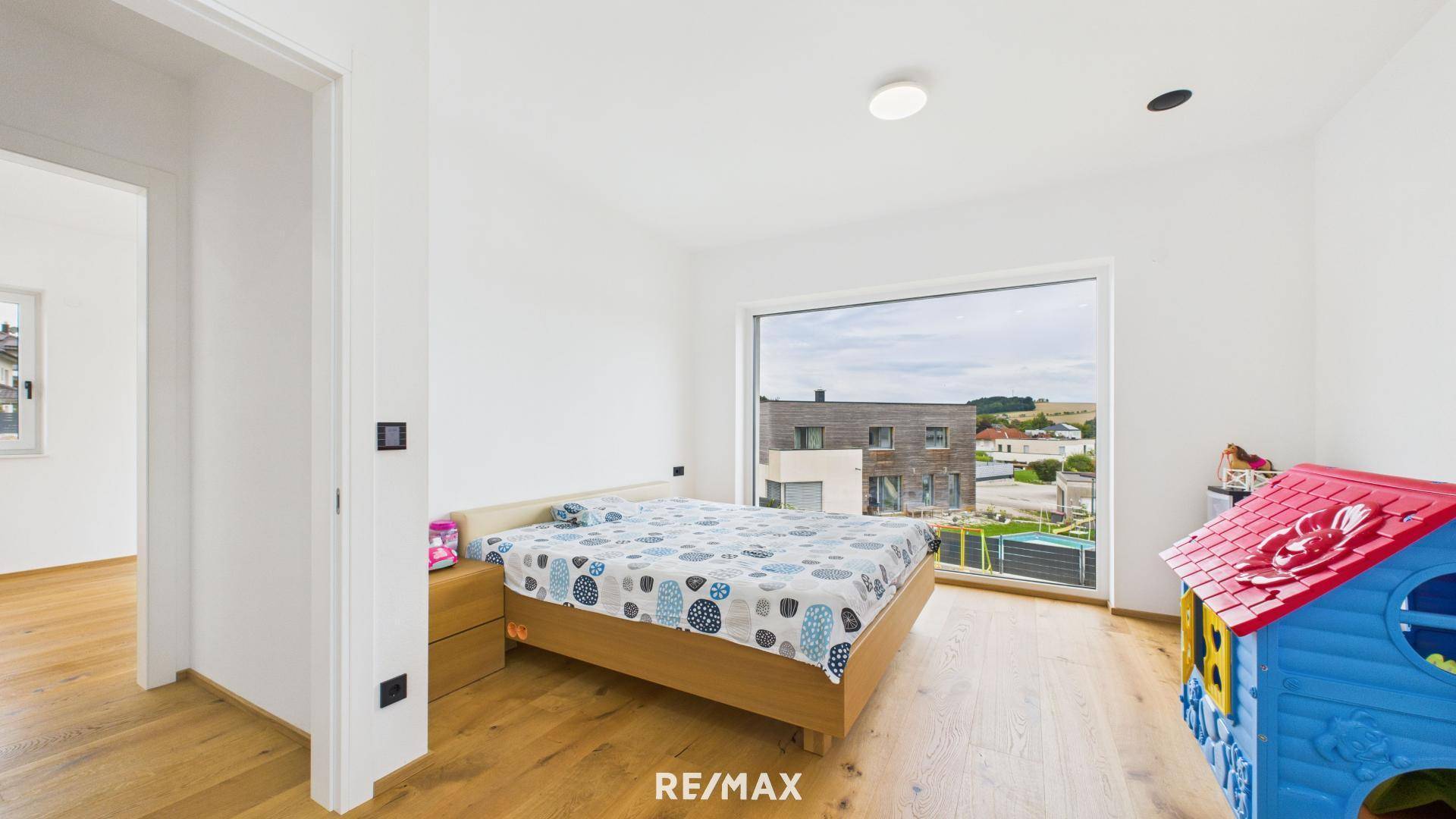 Helles Kinderzimmer mit Holzbett, Holzboden und großem Fenster mit Blick auf die Umgebung.