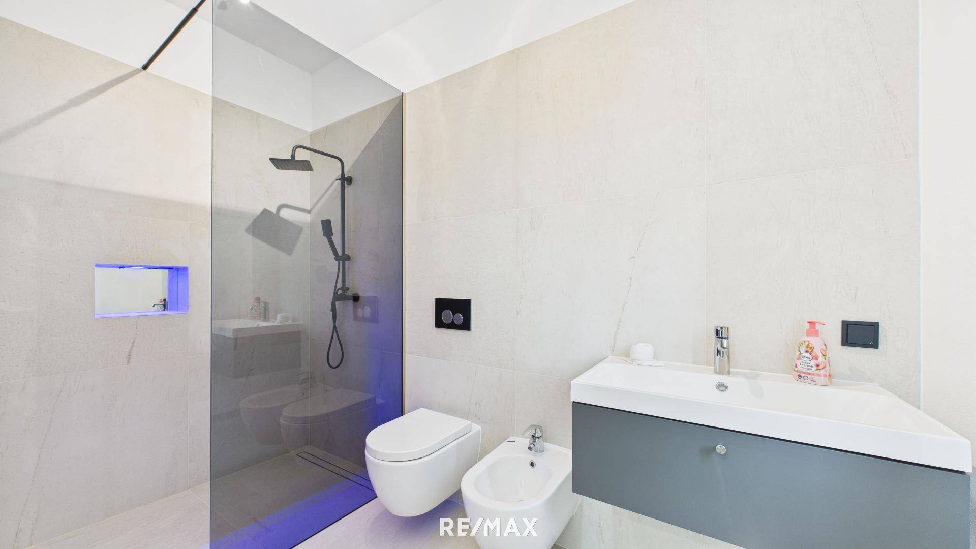 Modernes Badezimmer mit hellgrauen Fliesen, begehbarer Dusche, wandhängendem WC und Bidet.
