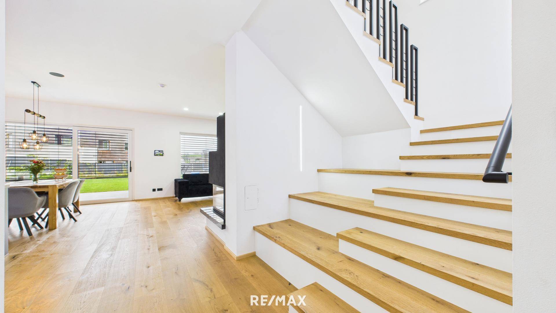 Moderne Holztreppe mit schwarzem Geländer, die den offenen Wohnbereich mit dem Obergeschoss verbindet.