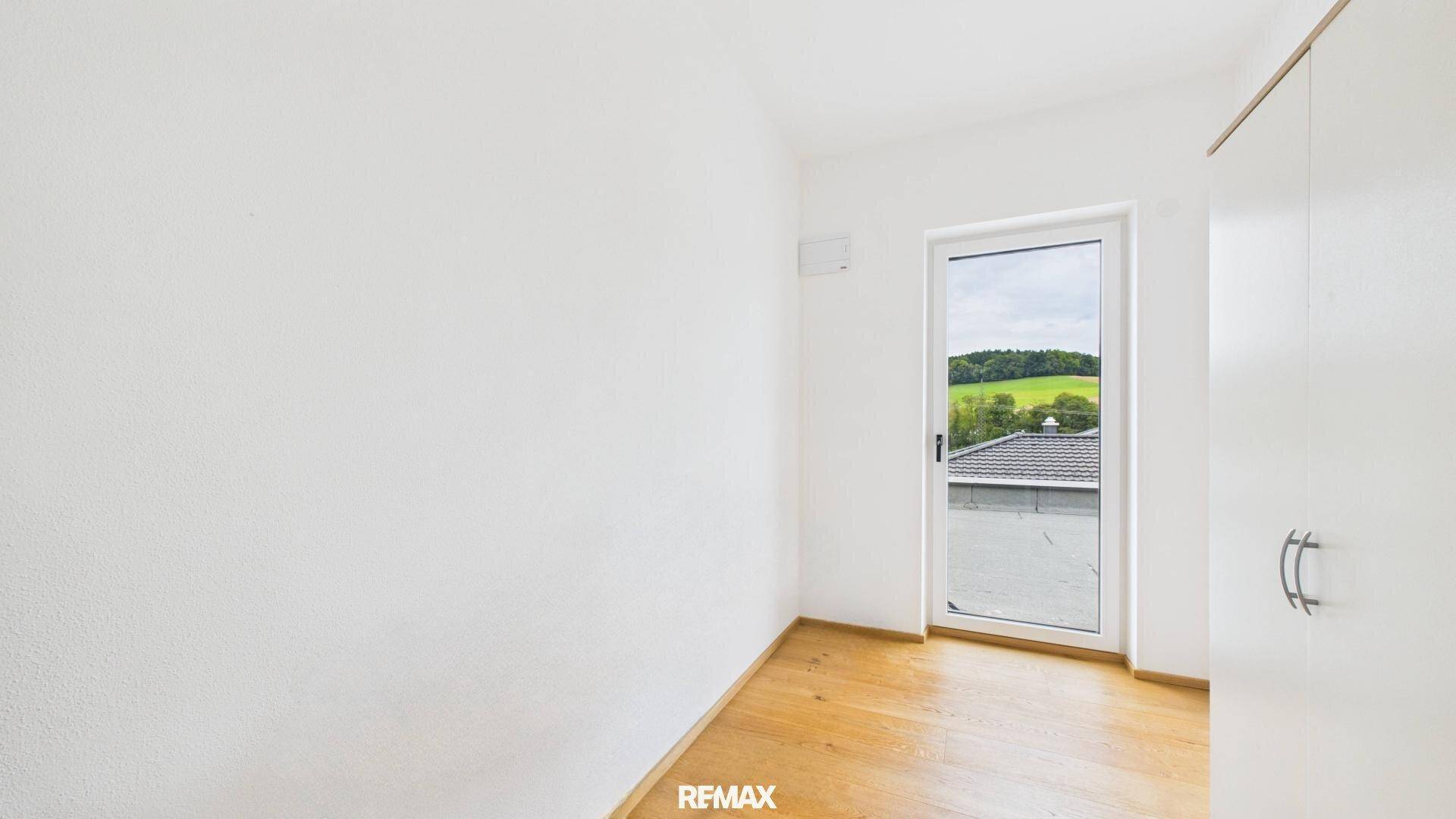 Helles Zimmer mit Holzboden und Fenster, das einen Blick auf die grüne Landschaft bietet.
