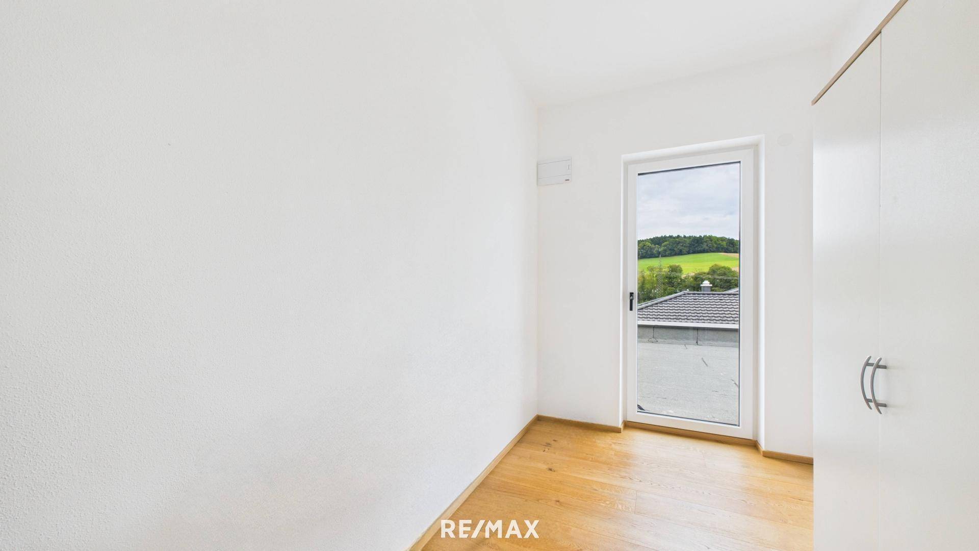 Helles Zimmer mit Holzboden und Zugang zu einem Außenbereich, bietet einen weiten Blick ins Grüne.