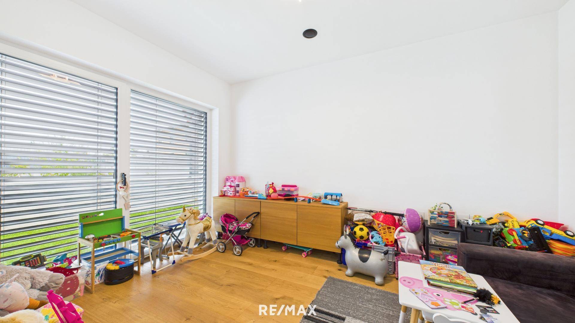 Helles Kinderzimmer mit Spielzeug, Holzschrank und großem Fenster mit Blick ins Grüne.
