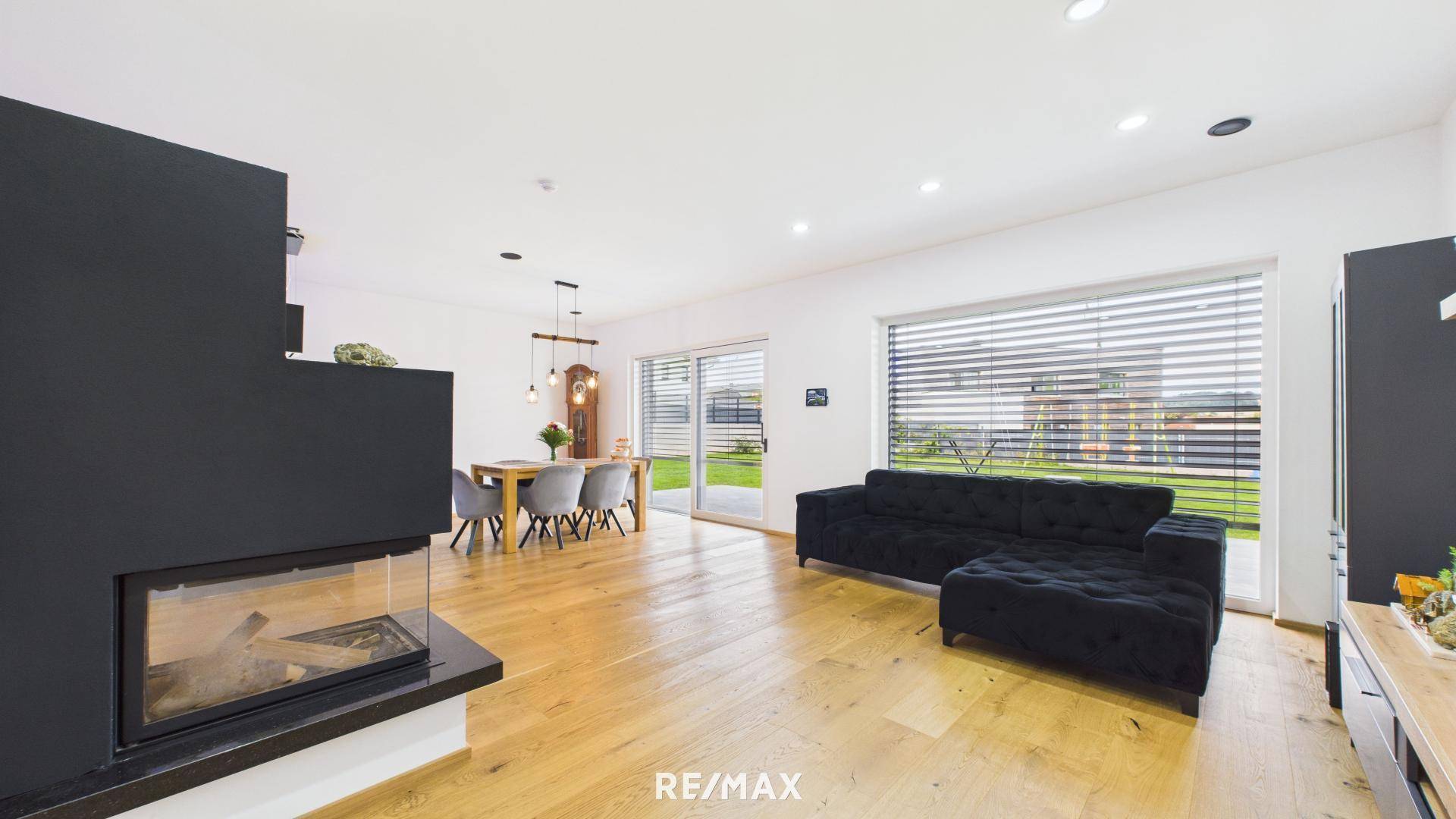 Gemütliches Wohnzimmer mit schwarzem Sofa, modernem Kamin und großem Fenster zum Garten.