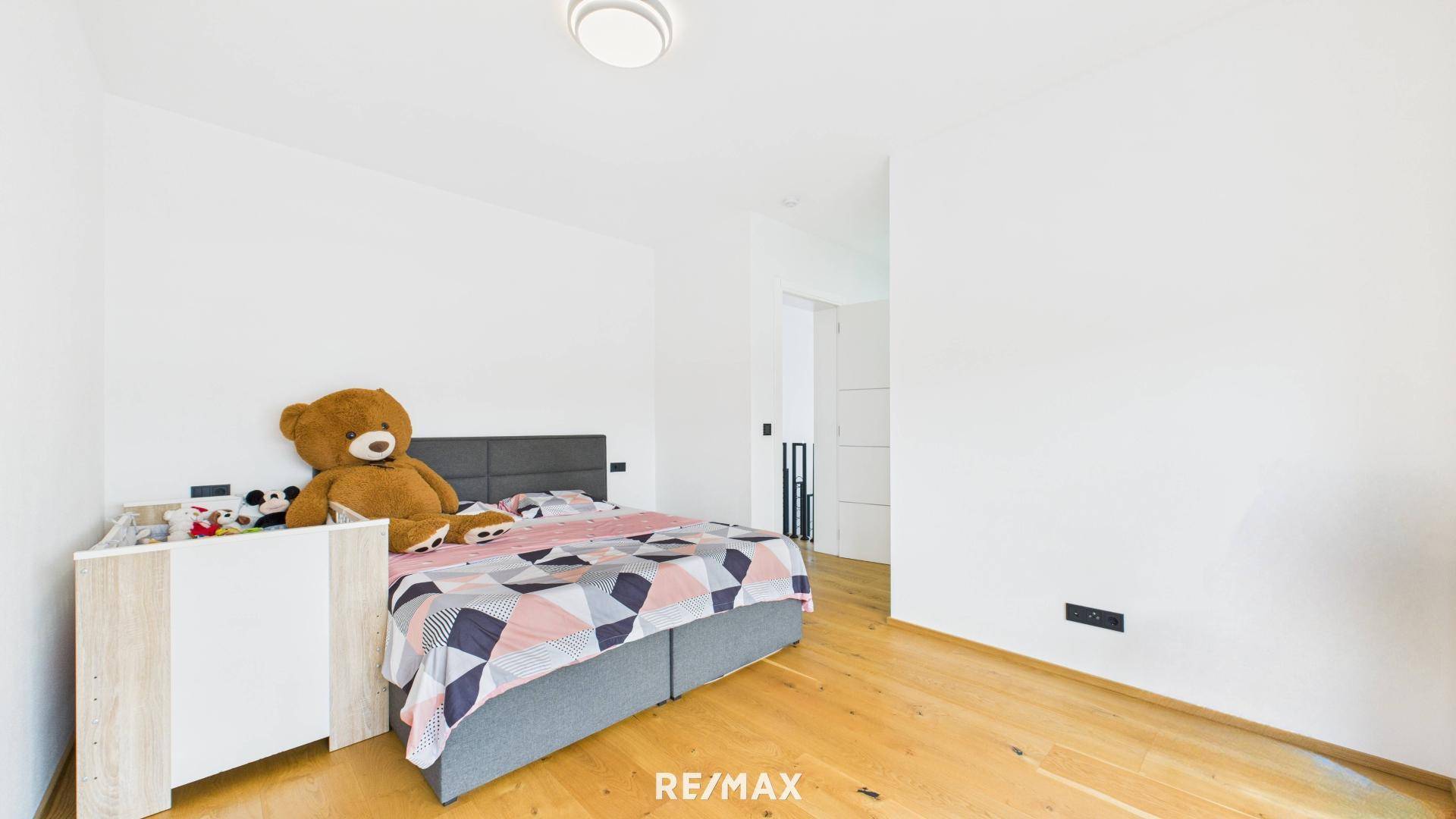 Gemütliches Schlafzimmer mit Holzboden und einem großen Teddybären auf dem Bett, hell und einladend.