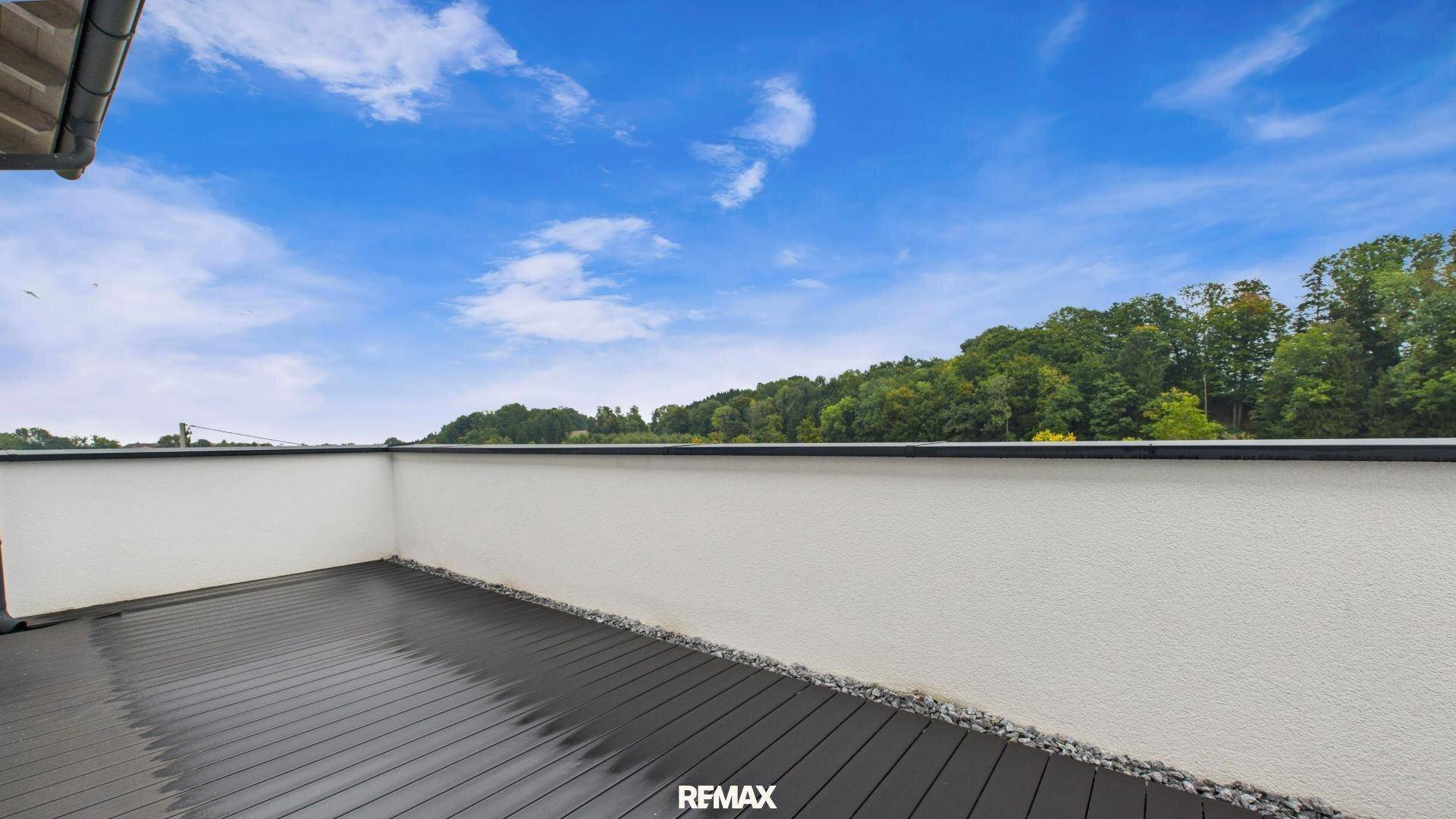 Geräumiger Balkon mit dunklem Holzboden und weitem Blick ins Grüne.