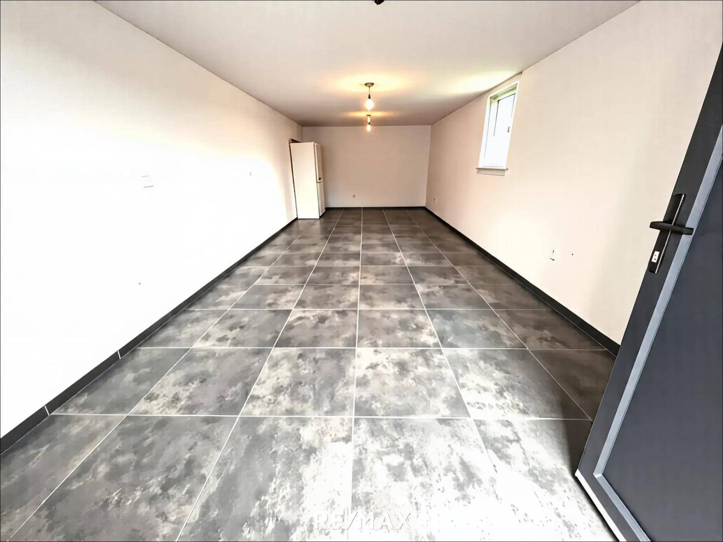 Geräumiger Mehrzweckraum mit Fliesenboden, einem Fenster und einem Kühlschrank.